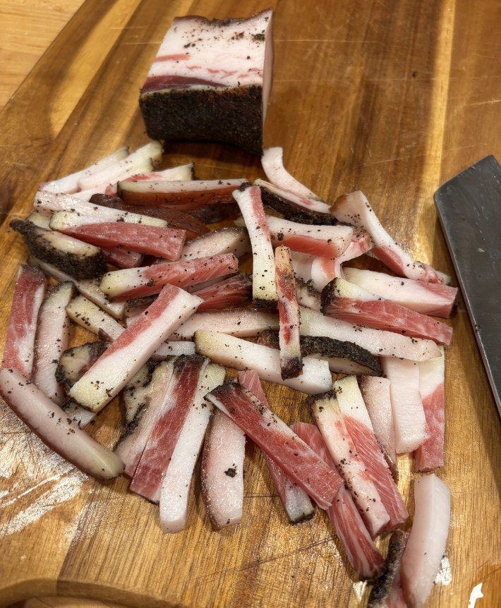 Freshly sliced guanciale on a wooden cutting board.