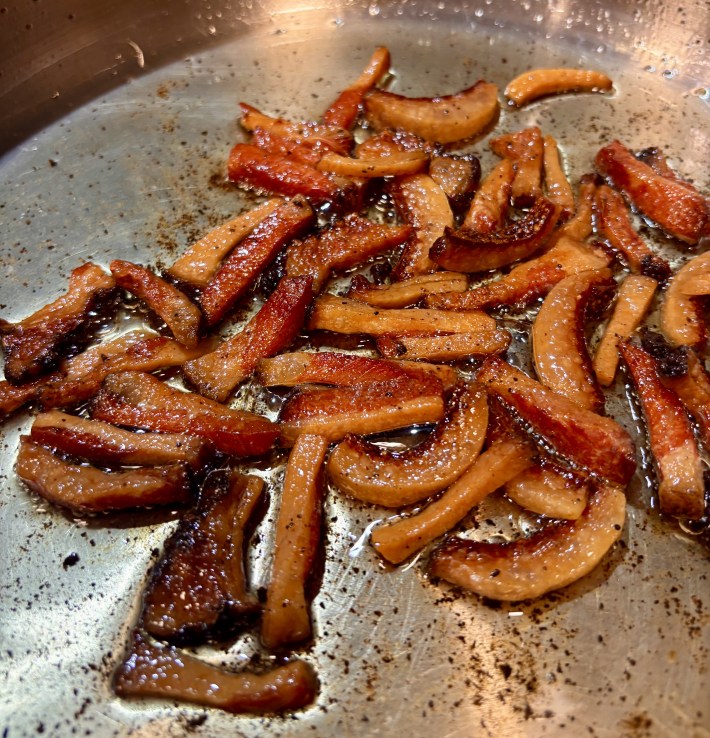 Sizzling guanciale strips cooking in a pan.