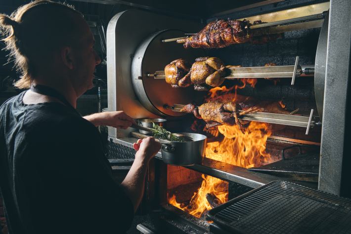 Chef Marc Forgione bastes whole animals roasting on a wood-fired rotisserie at Peasant