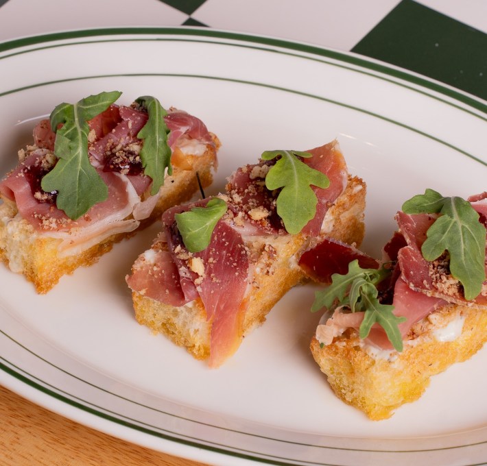 Prosciutto crostini with arugula on white plate