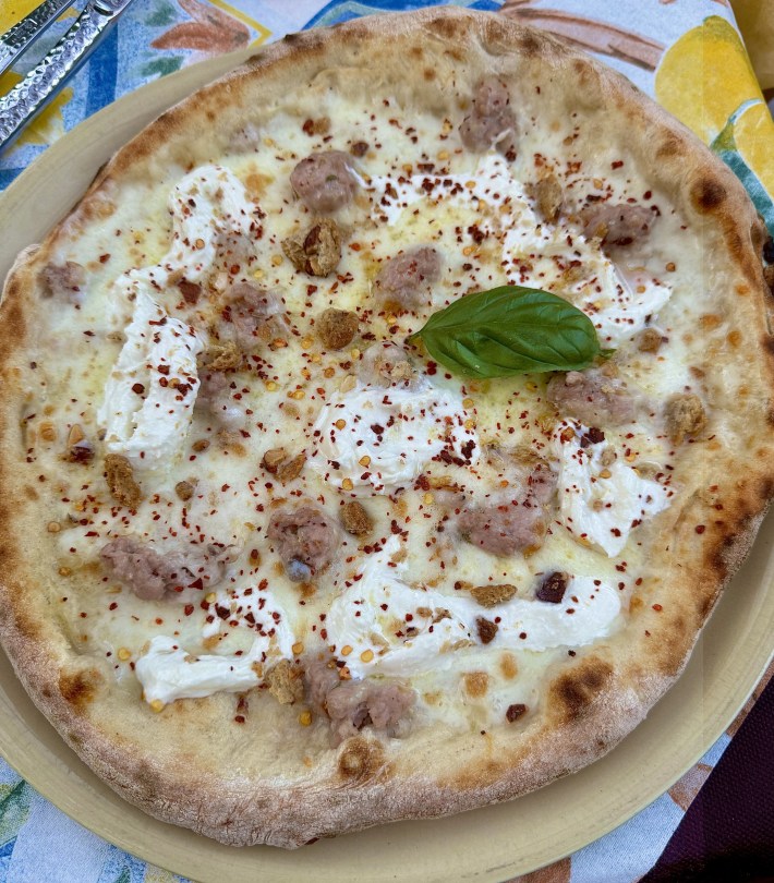 Rustica pizza with golden crust, topped with a basil leaf on a bright tablecloth.