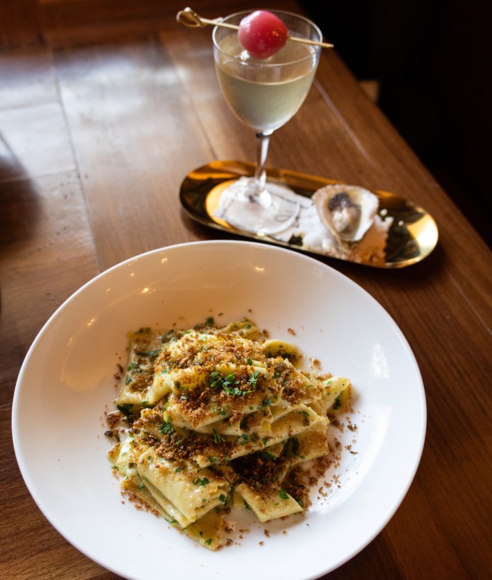 Plate of pasta made from ravioli scraps with anchovy crunch, served alongside an oyster martini cocktail.