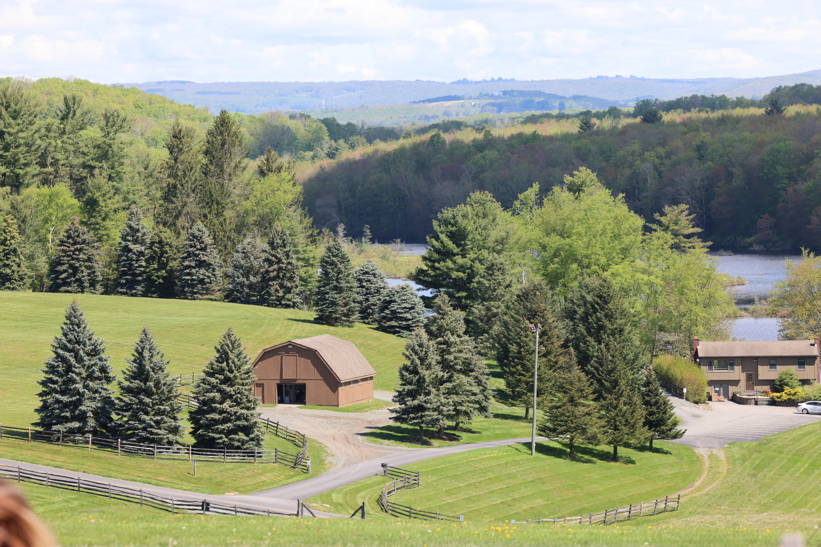 Rolling green hills and barns in the Sullivan Catskills with a lake in the background.