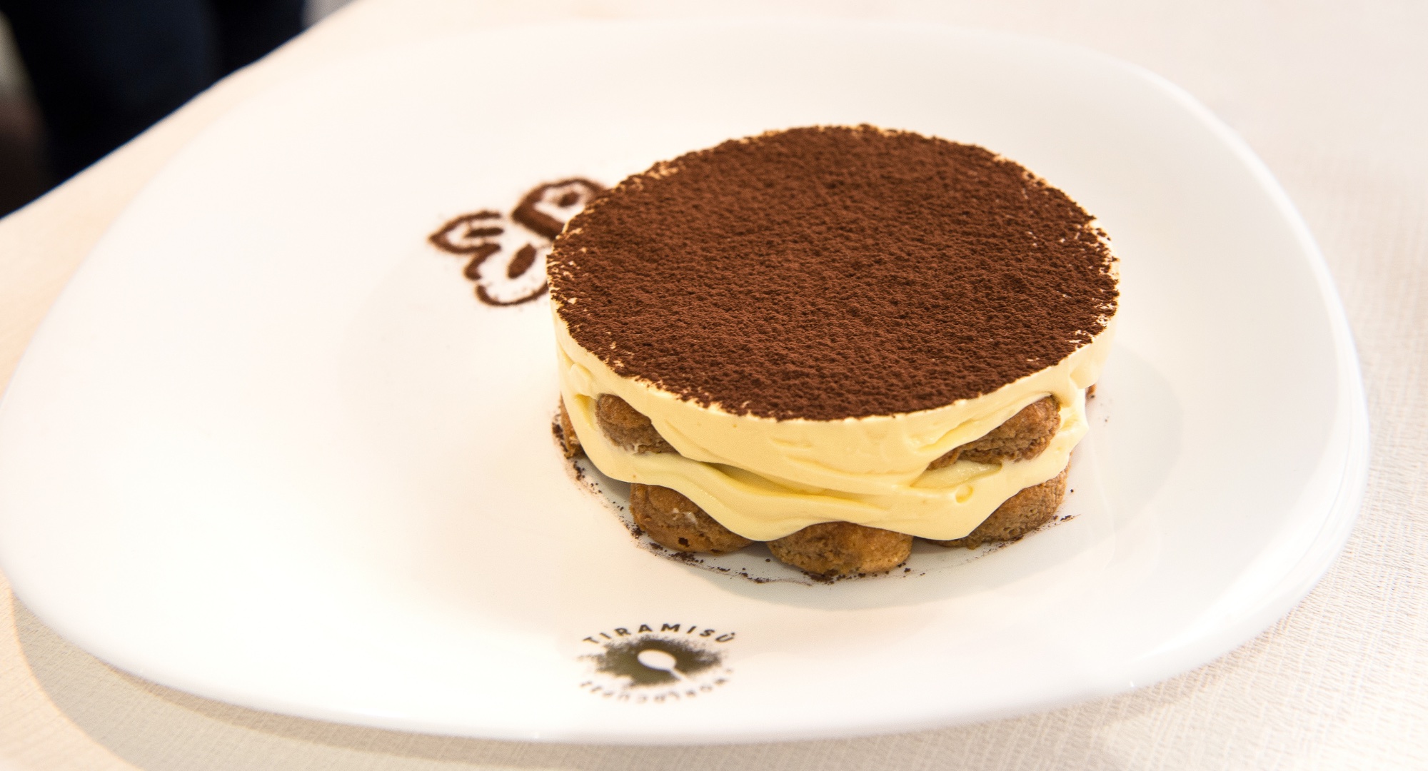 Tiramisu layered and topped with cocoa on a white plate with the Tiramisu World Cup logo.