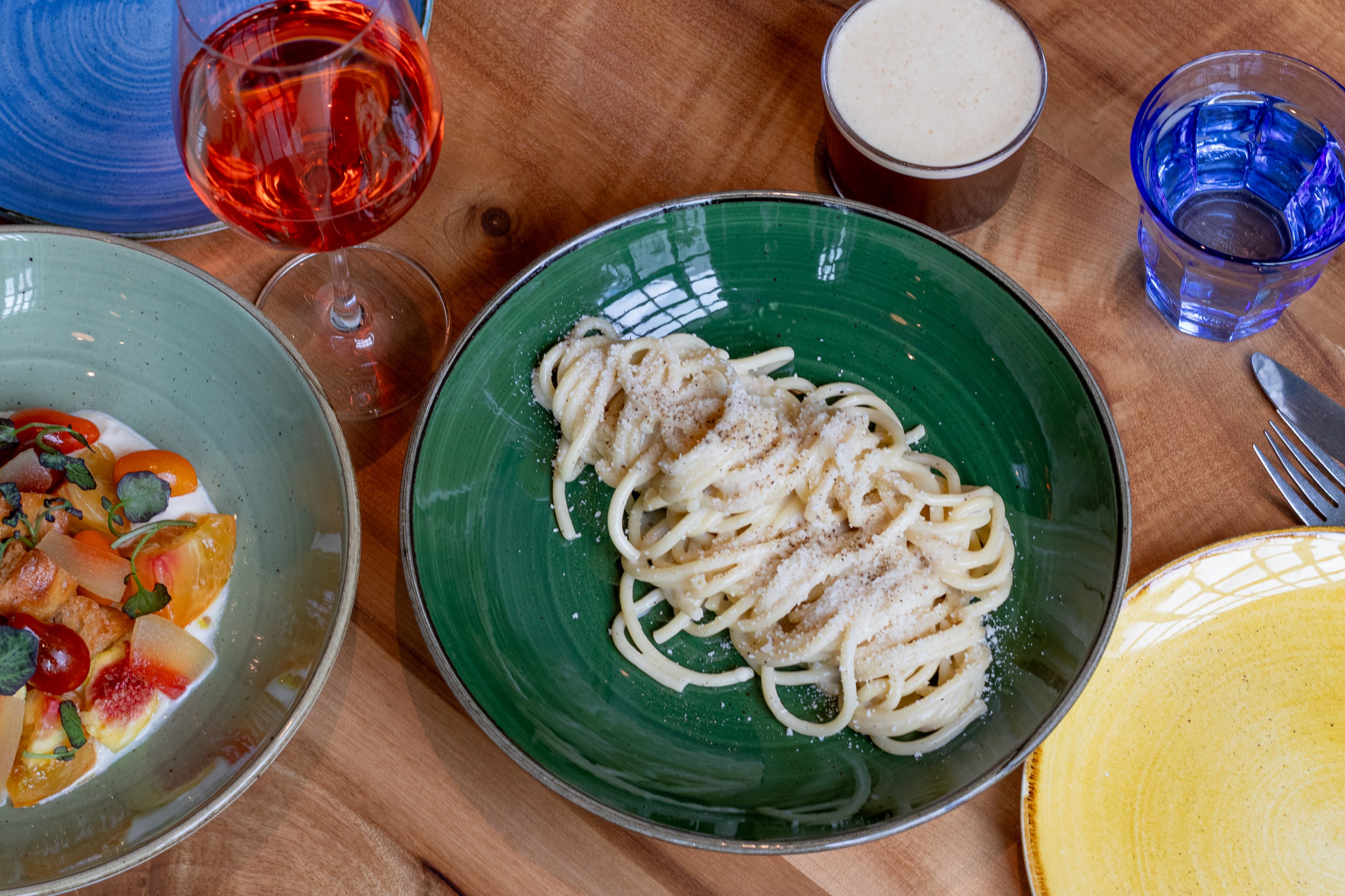 Bucatini cacio e pepe served in a green bowl, with wine, water and coffee, photo by Isabel Baer.
