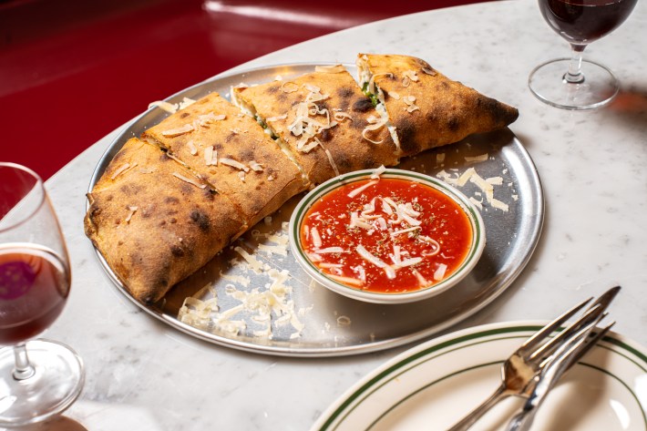 Golden calzone on a plate with tomato dipping sauce and glasses of red wine.