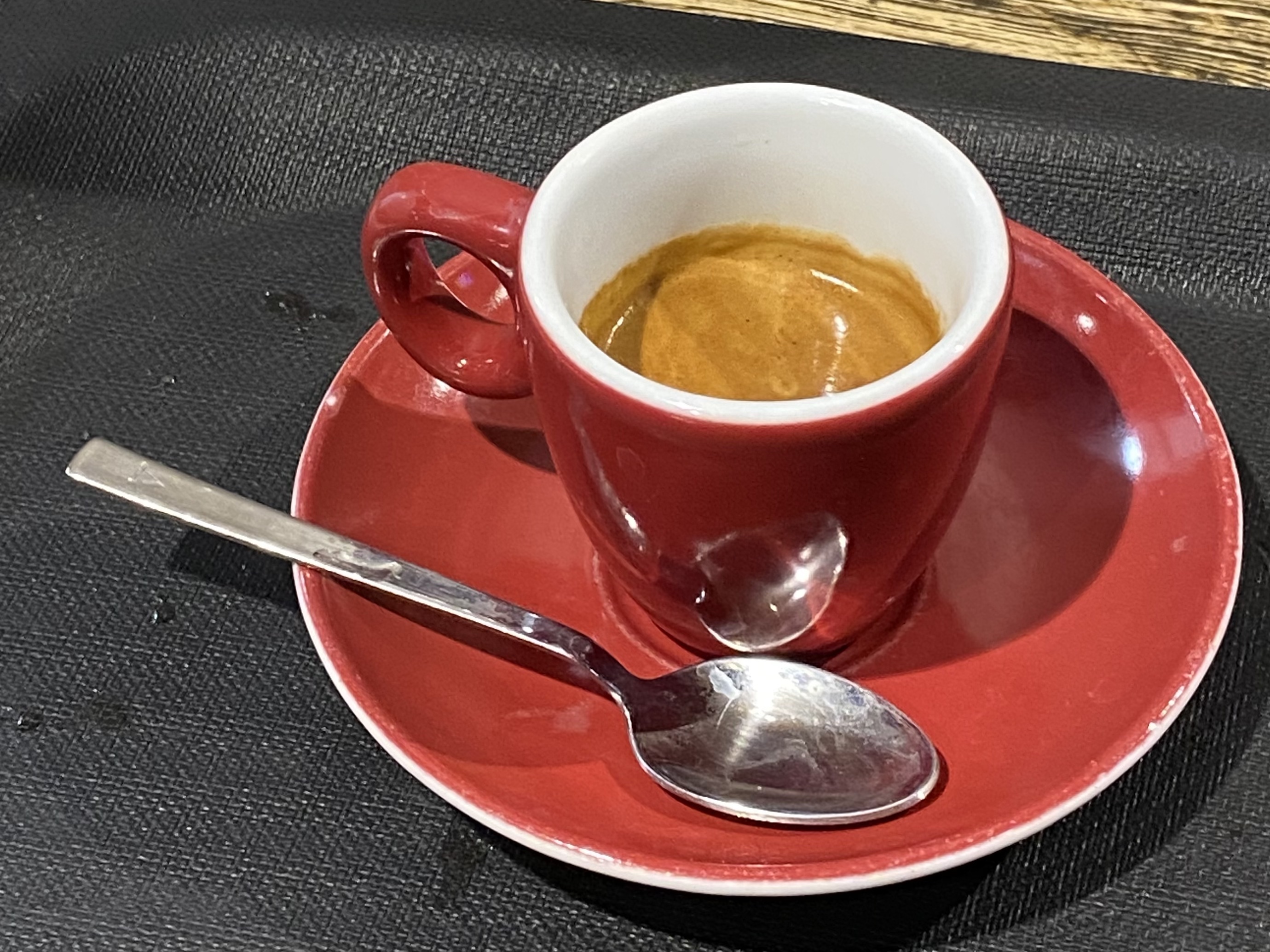 A small red cup of Italian espresso on a red saucer with a spoon