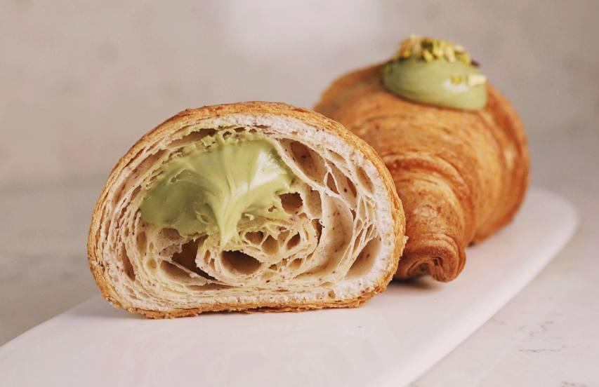 Flaky gluten-free cornetto topped with green pistachio cream, cut in half.
