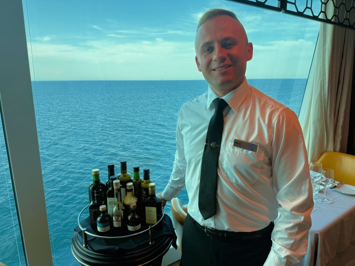 Olive oil concierge Mihai presenting a cart of premium extra virgin olive oils aboard Oceania’s Allura