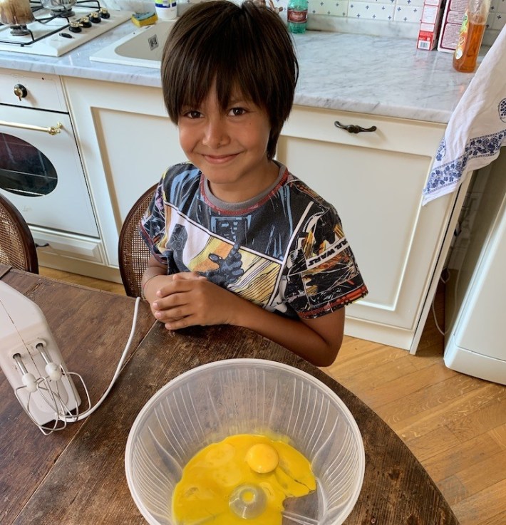 Gregorio making pizza dough in the kitchen, with a bowl of beaten eggs in front of him.