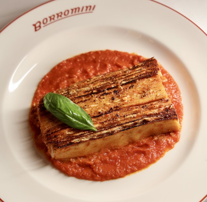 Rectangular slice of 100-Layer Lasagna on tomato sauce topped with a basil leaf, served at Borromini.
