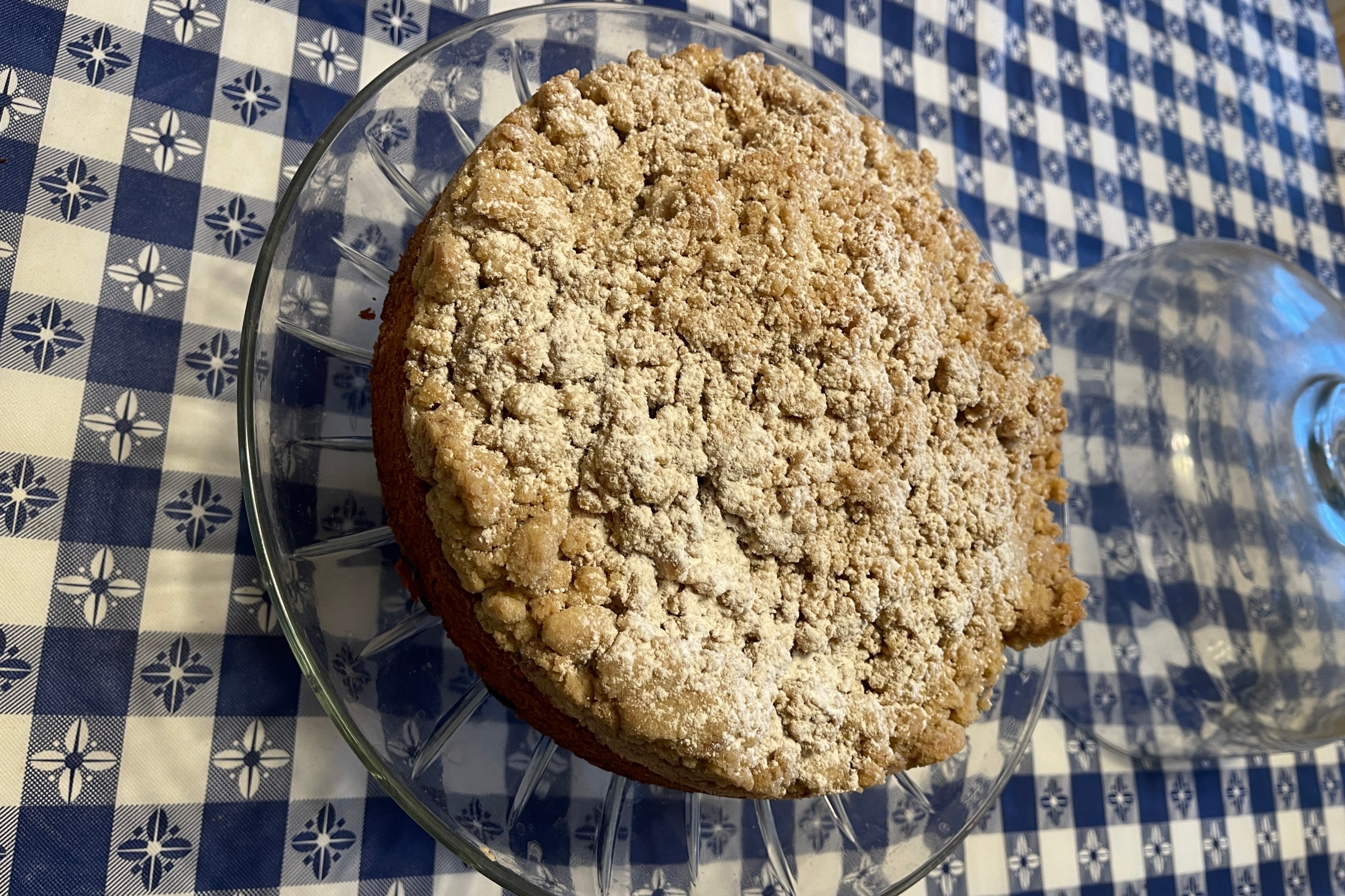 Grandma's homemade crumb cake topped with buttery crumbs on a glass cake stand