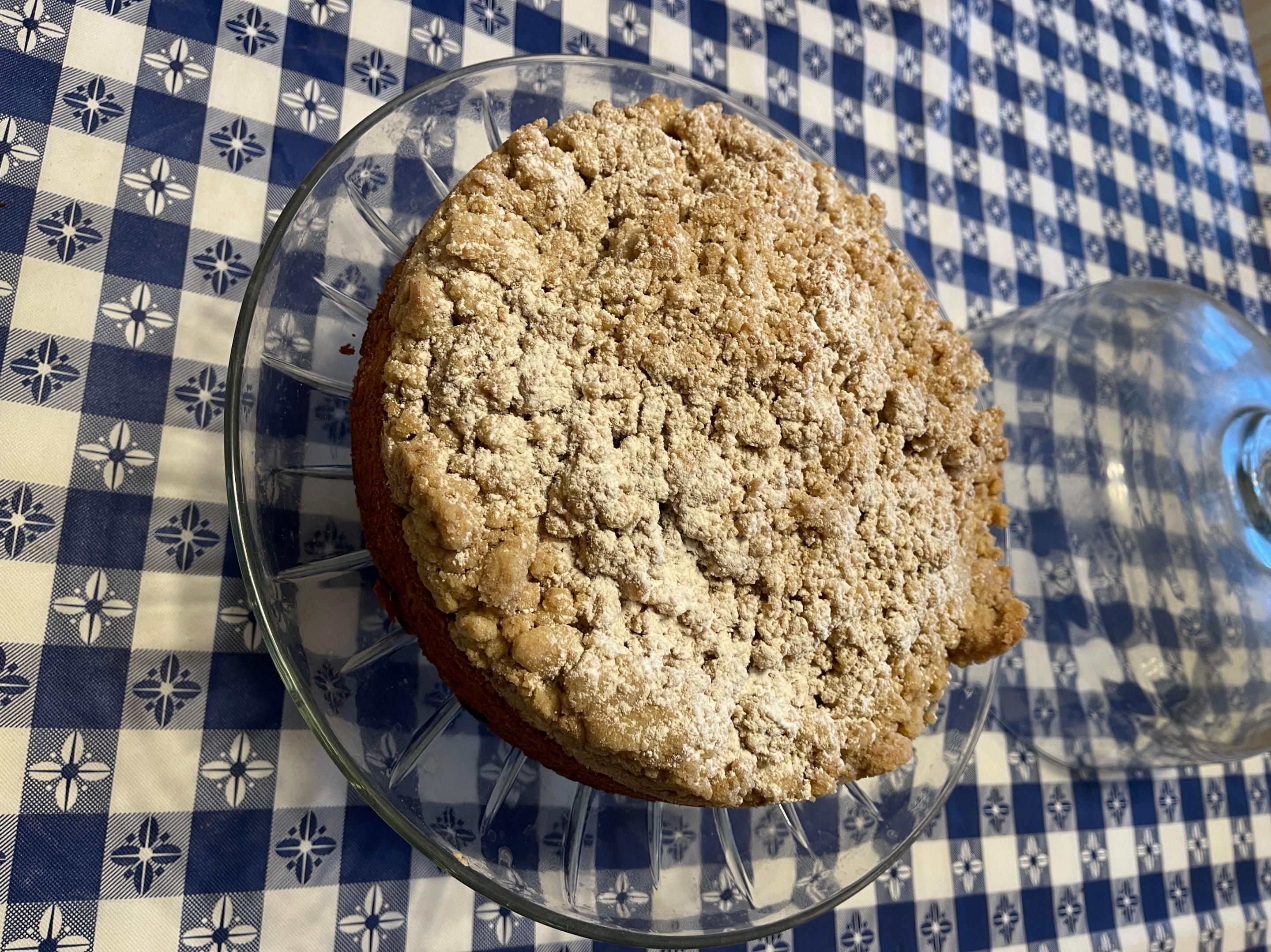 Grandma's homemade crumb cake topped with buttery crumbs on a glass cake stand