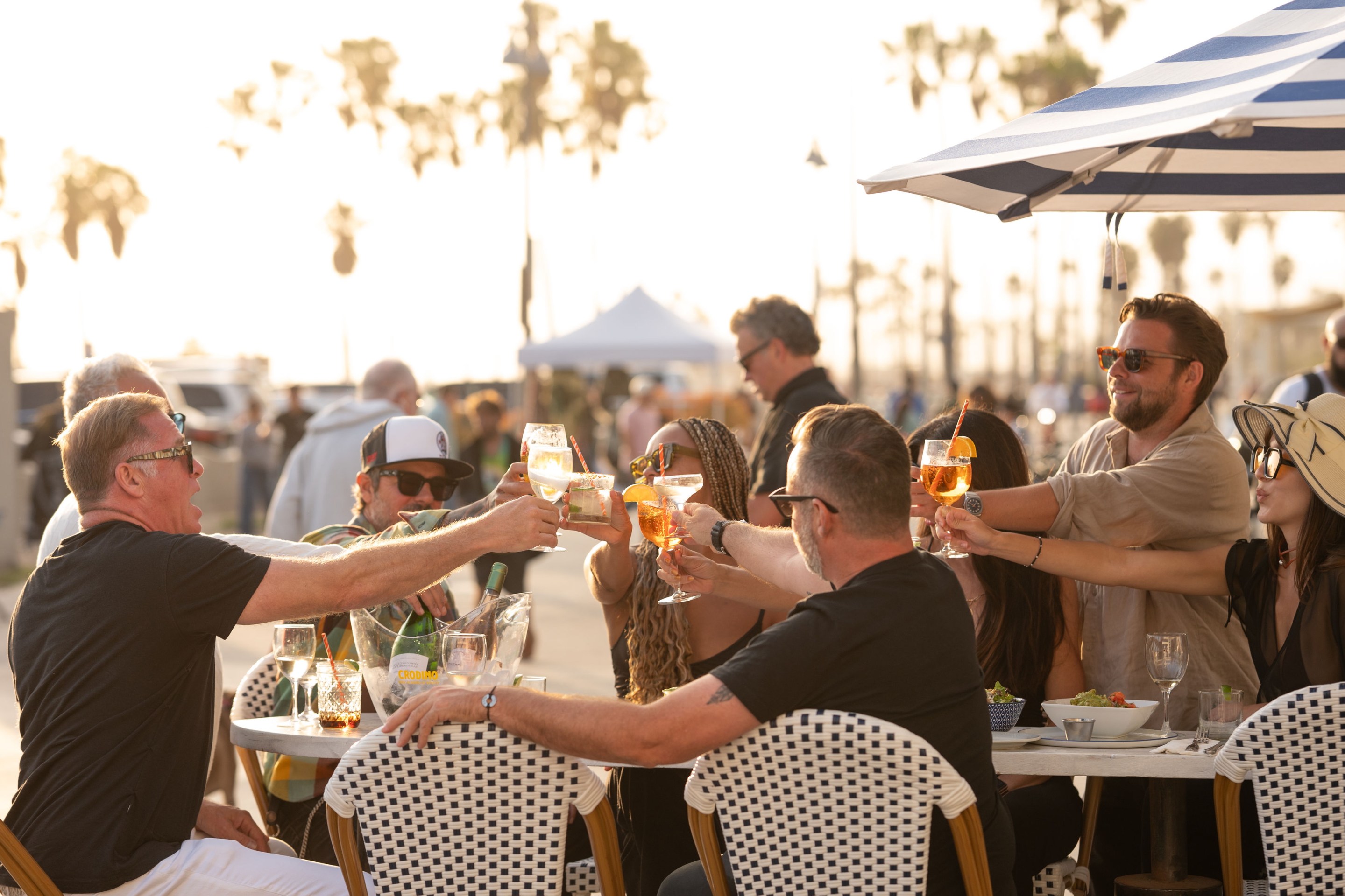 Guests enjoying spritz cocktails and shared plates outdoors at Venice Beach Club along the Venice Boardwalk.