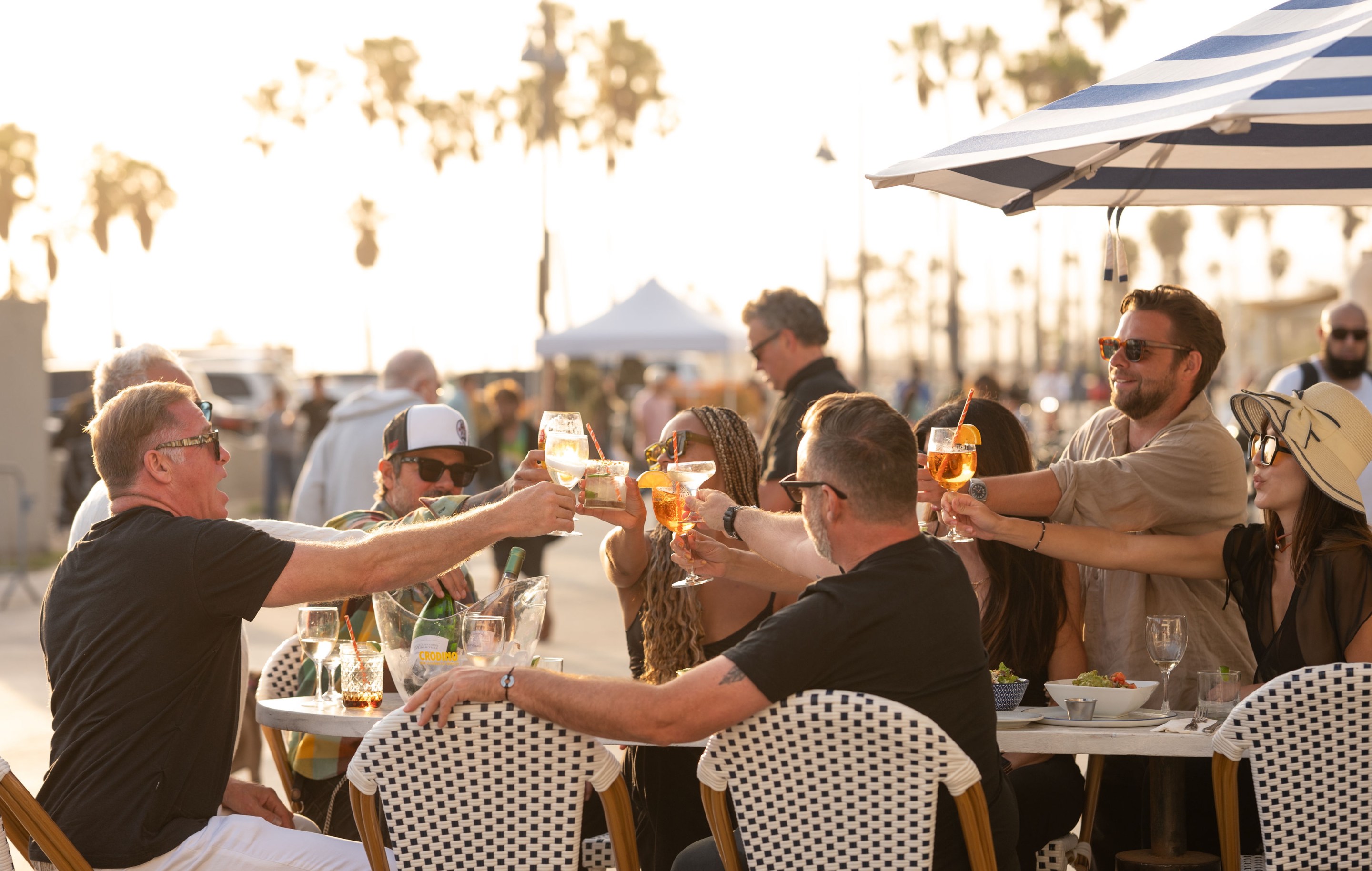 Guests enjoying spritz cocktails and shared plates outdoors at Venice Beach Club along the Venice Boardwalk.
