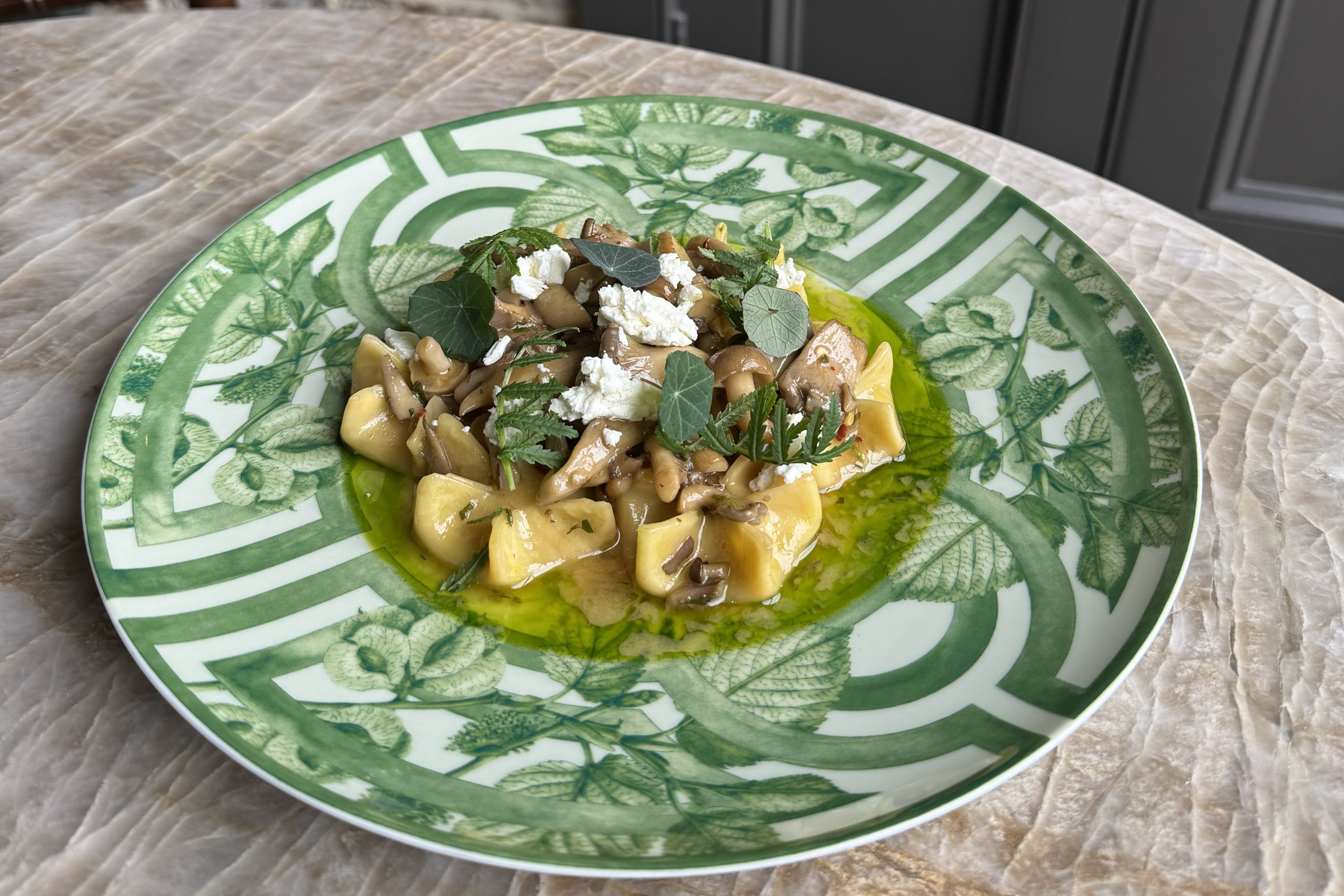 Sacchetti pasta with mushroom ragout and goat cheese at Legami Charleston, served on a green patterned plate with fresh herbs and olive oil.