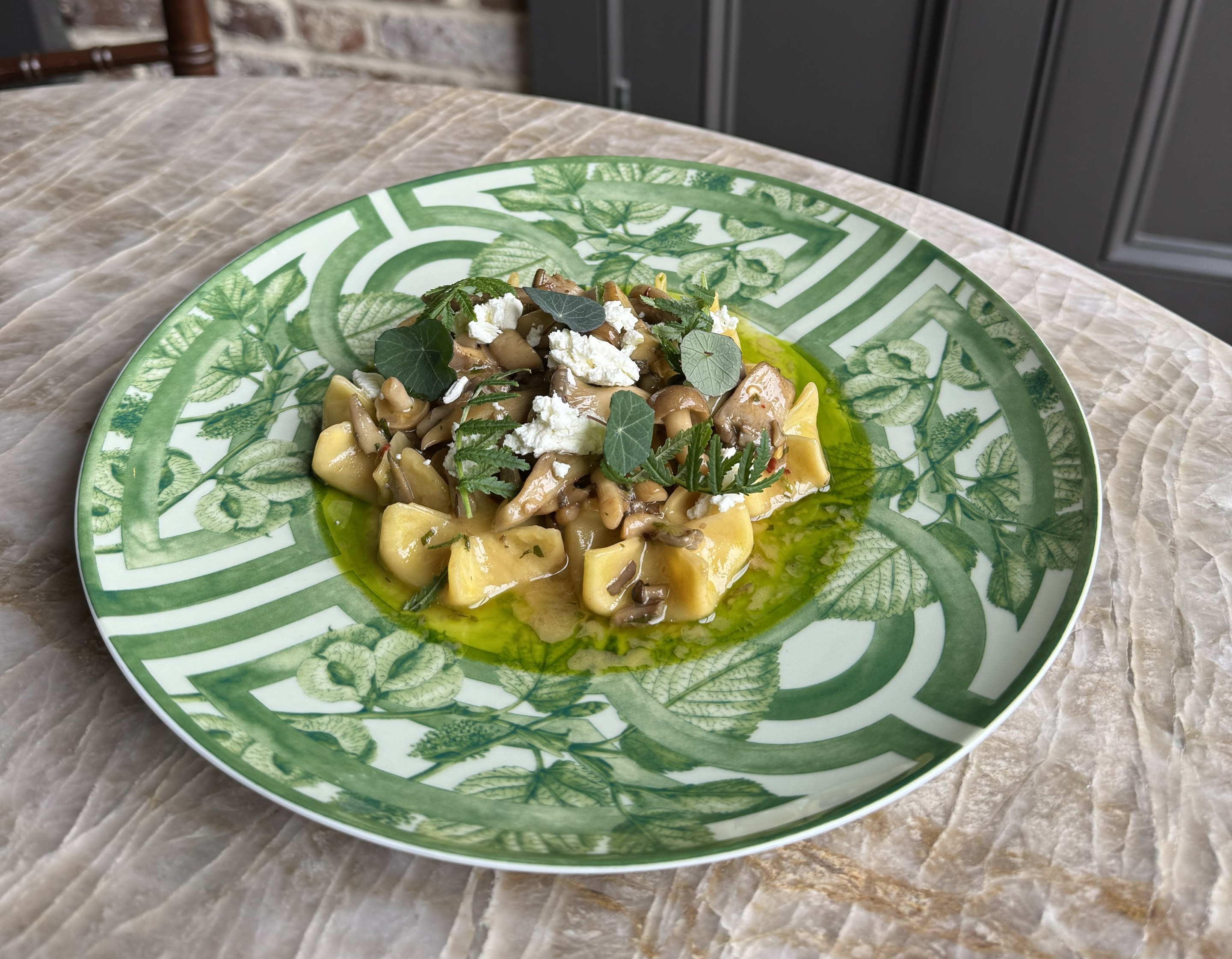 Sacchetti pasta with mushroom ragout and goat cheese at Legami Charleston, served on a green patterned plate with fresh herbs and olive oil.