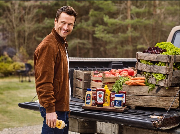 Glen Powell with Smash Kitchen condiments at a farm stand.