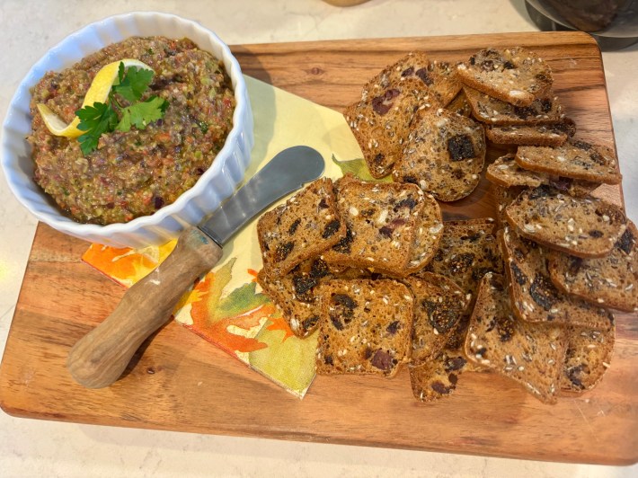 Close-up of Sicilian olive tapenade with lemon twist and parsley, served with crackers.