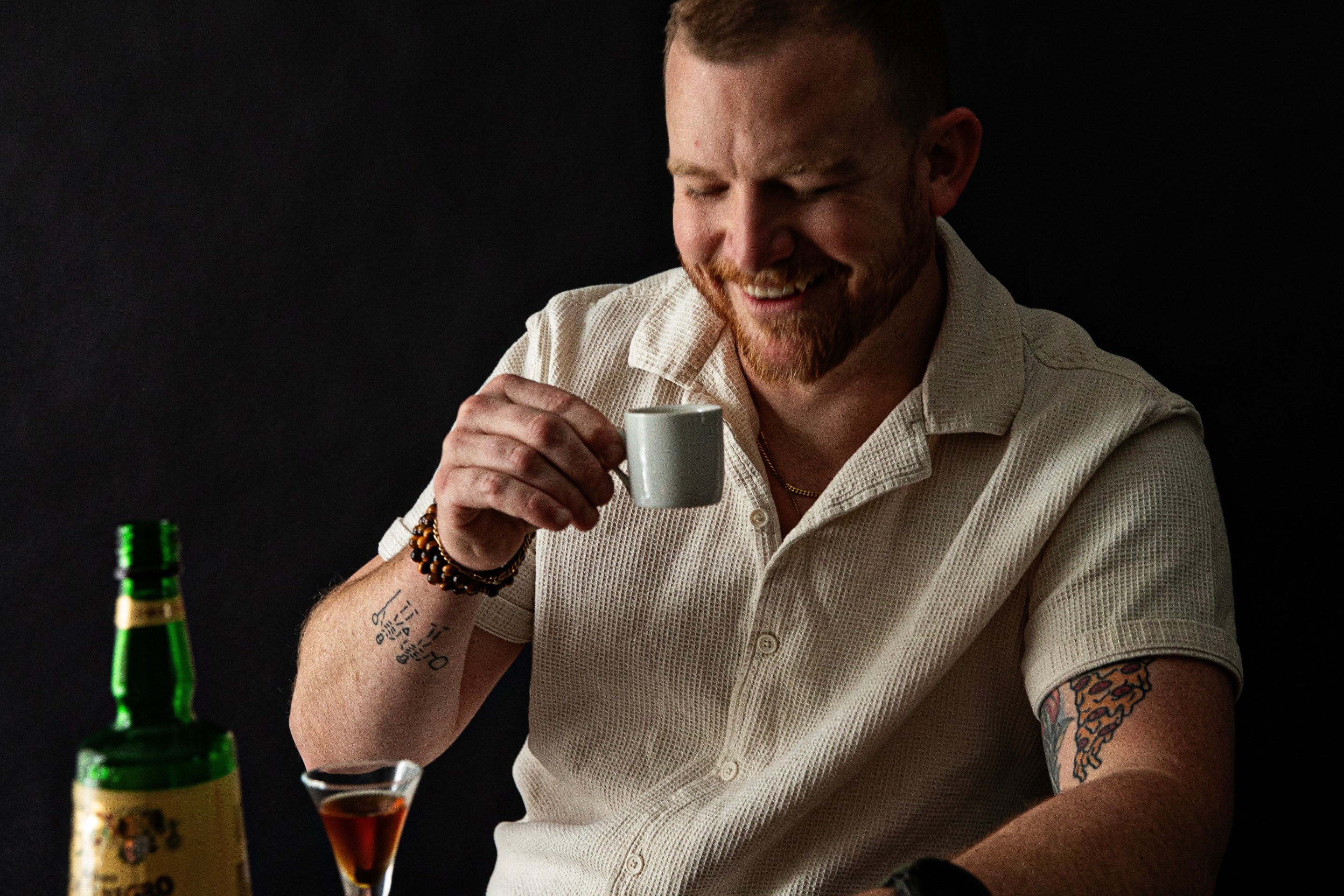 Chef Mark Bolchoz smiling while holding an espresso cup at a table.