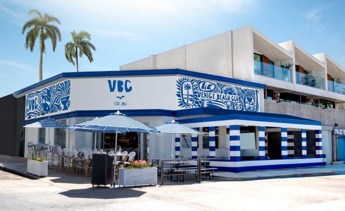 Exterior of Venice Beach Club in Los Angeles, featuring blue-and-white design and striped patio umbrellas.