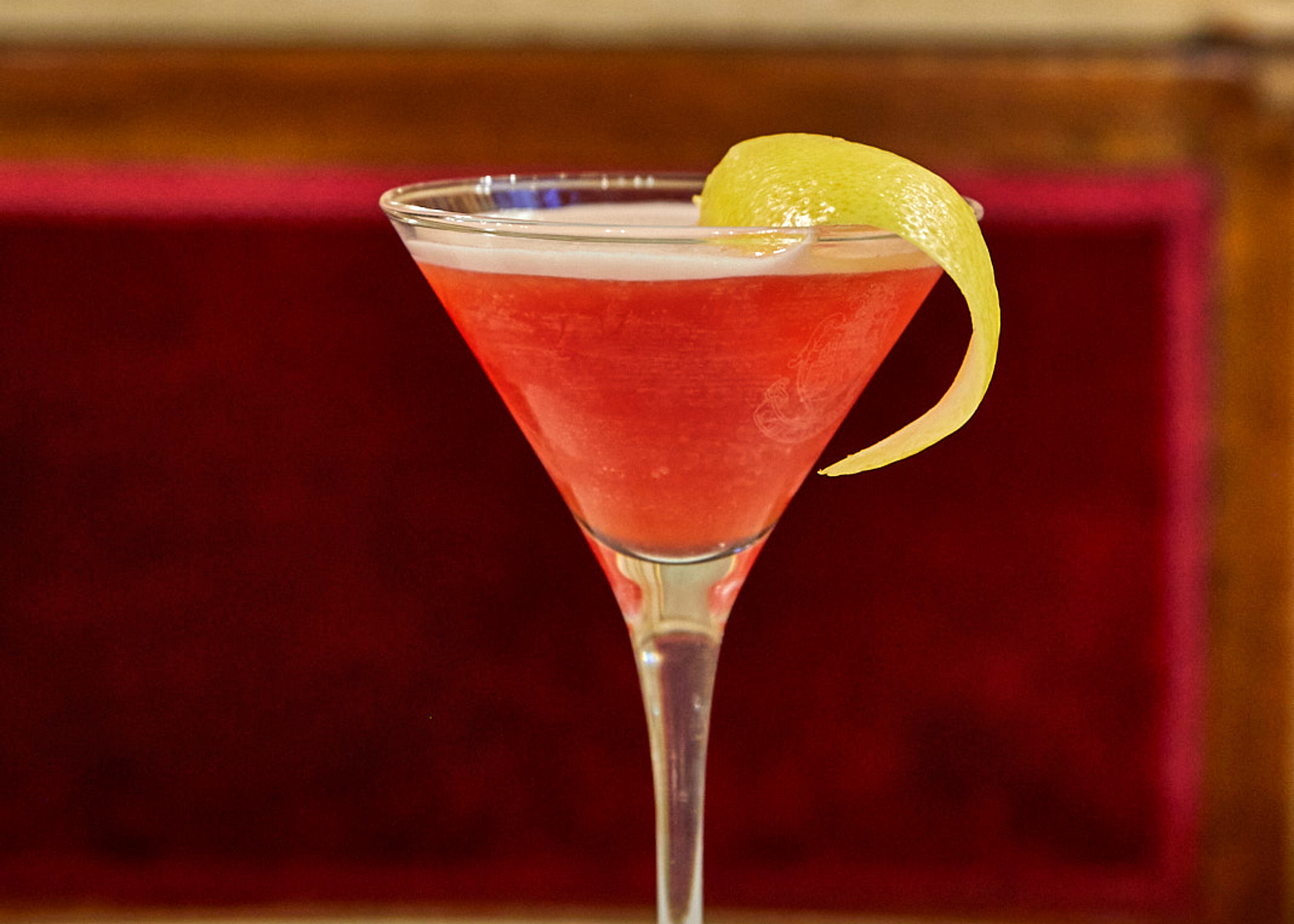 Red amaro cocktail with a citrus twist in a martini glass.