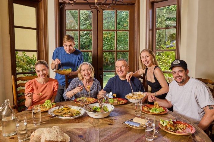 Phil Rosenthal and family gather around a dining table sharing pasta and salad.