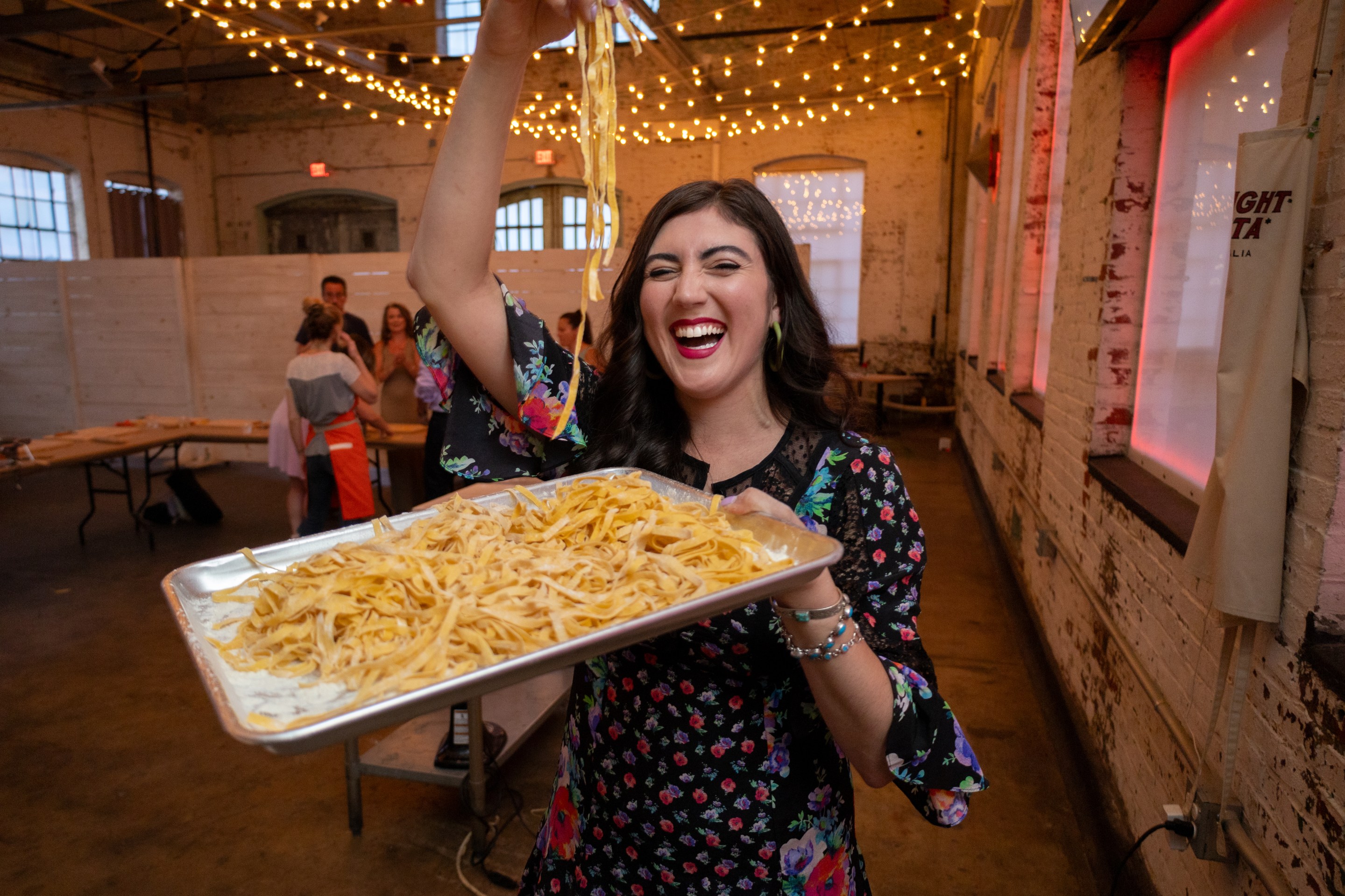 Natalia Lepore Hagan holding a tray of fresh pasta under string lights at Midnight Pasta in Philadelphia.