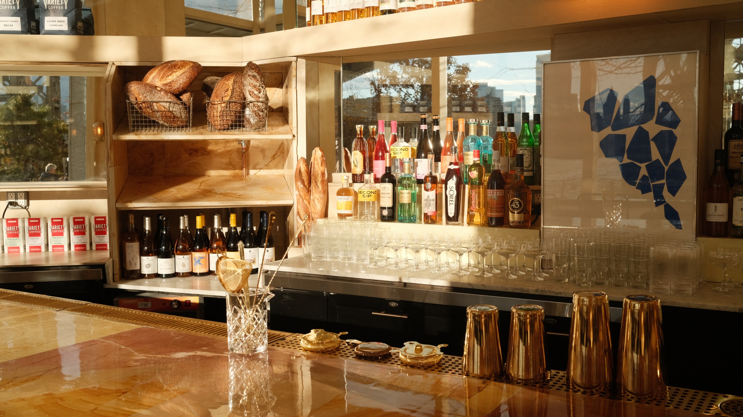 Bar at Cafe Susanne with loaves of bread, wine bottles and spirits lit by afternoon sun in front of the Brooklyn waterfront.