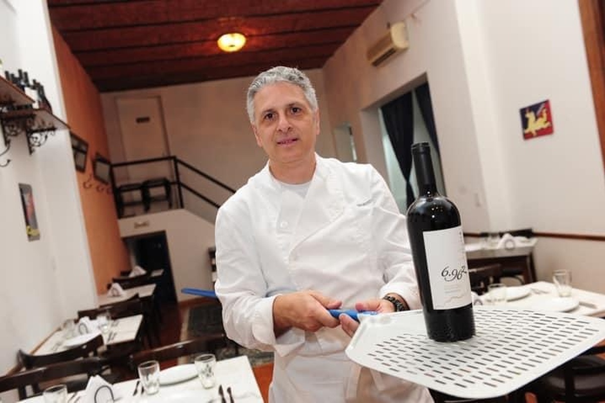 hef Maurizio de Rosa in white chef coat holding a bottle of wine inside his restaurant.