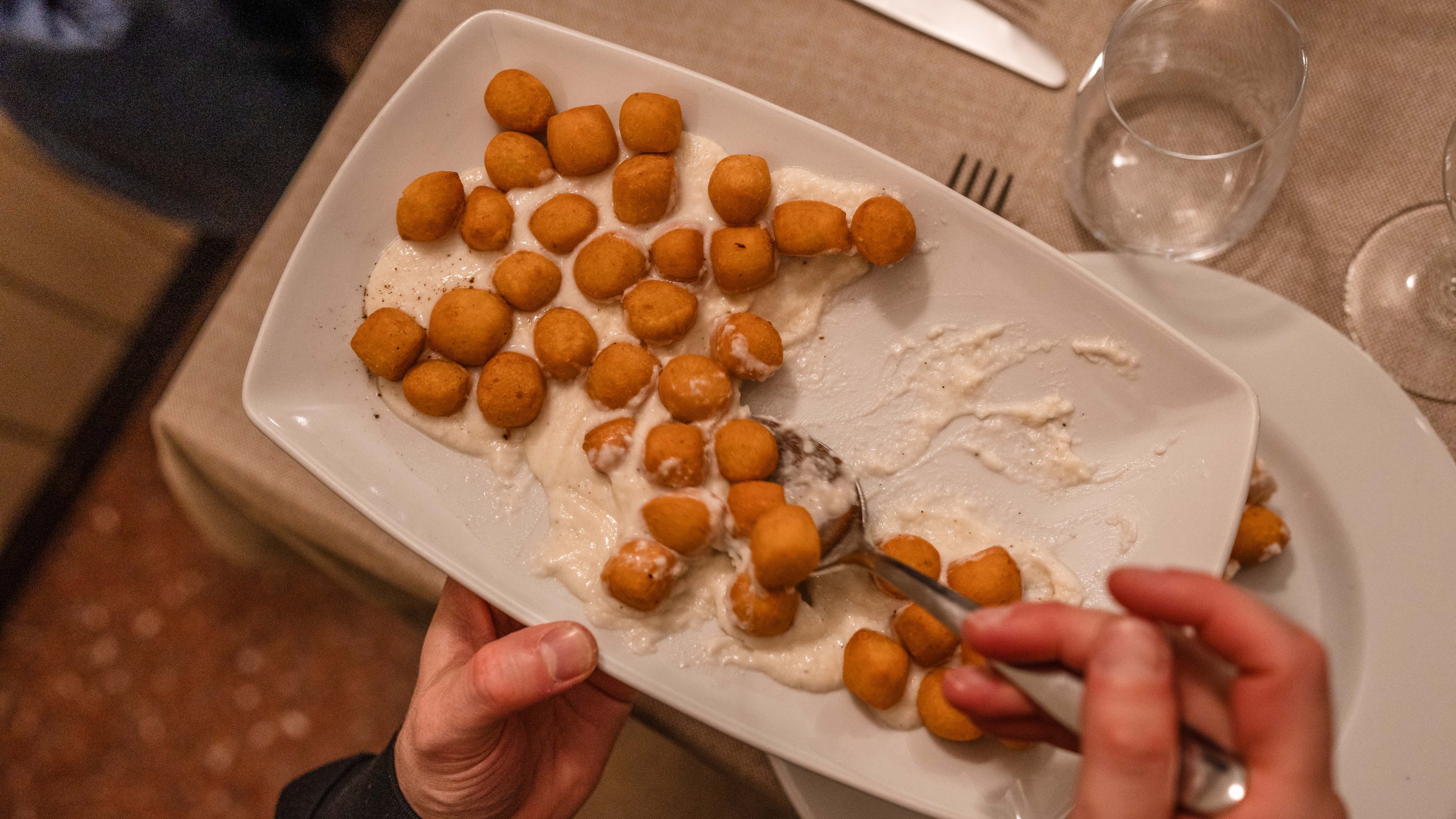 Fried gnocchi served over creamy cacio e pepe sauce on a white platter.
