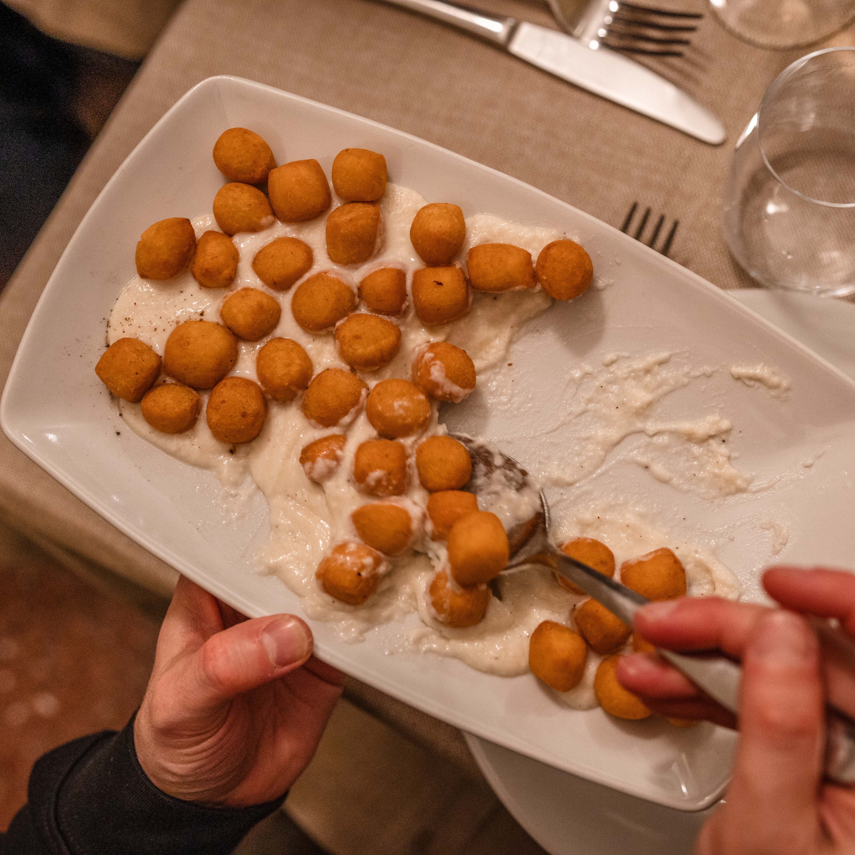 Fried gnocchi served over creamy cacio e pepe sauce on a white platter.