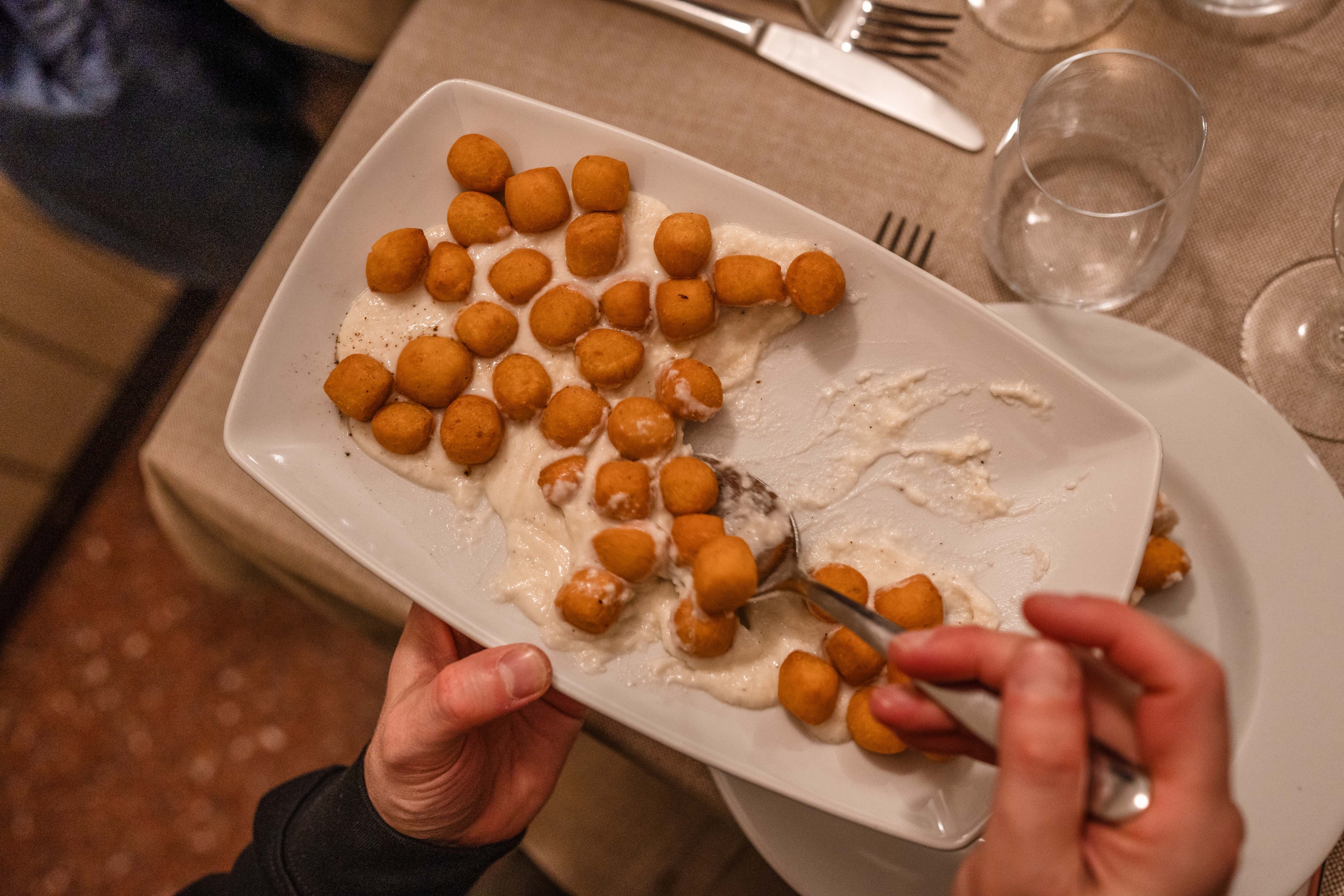 Fried gnocchi served over creamy cacio e pepe sauce on a white platter.