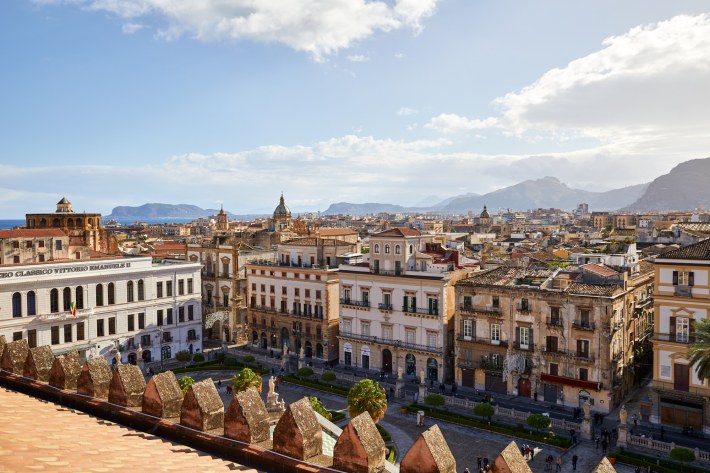 Rooftop view of Palermo with the sea and mountains in the distance.