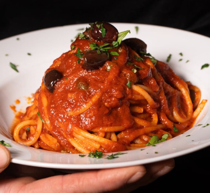 pasta all puttanesca at RUA Taverna Gastronomica topped with olives in a white bowl.