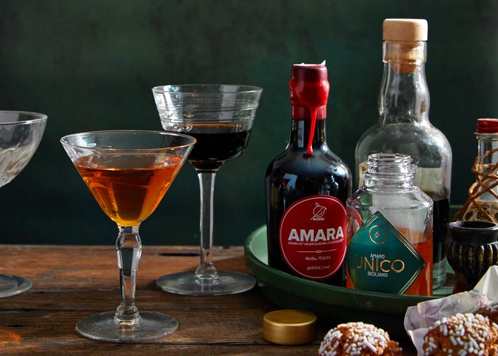 Bottles and glasses of Sicilian amari on a wooden table.