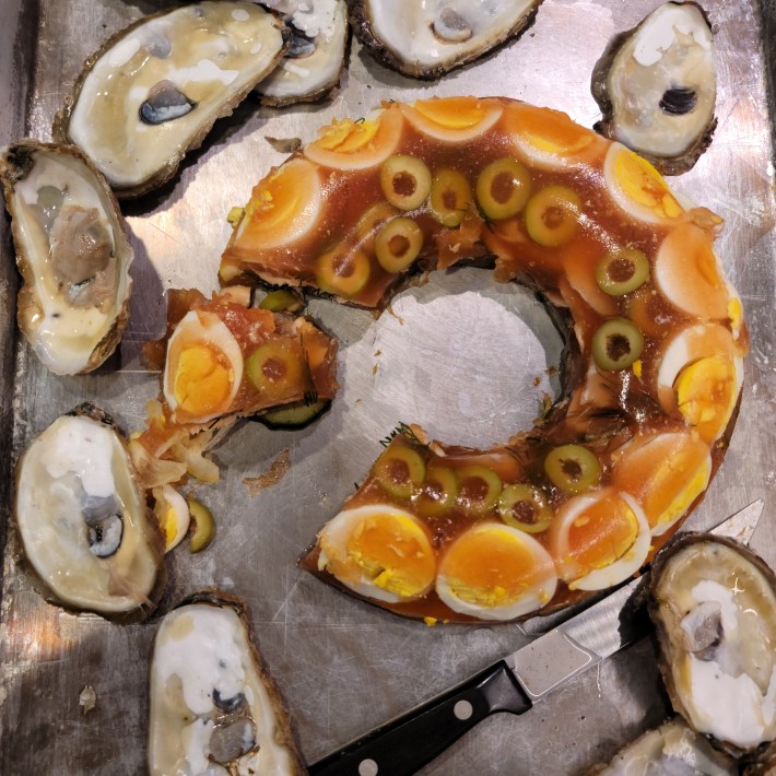 Savory aspic with sliced egg and green olives, served alongside freshly shucked oysters.