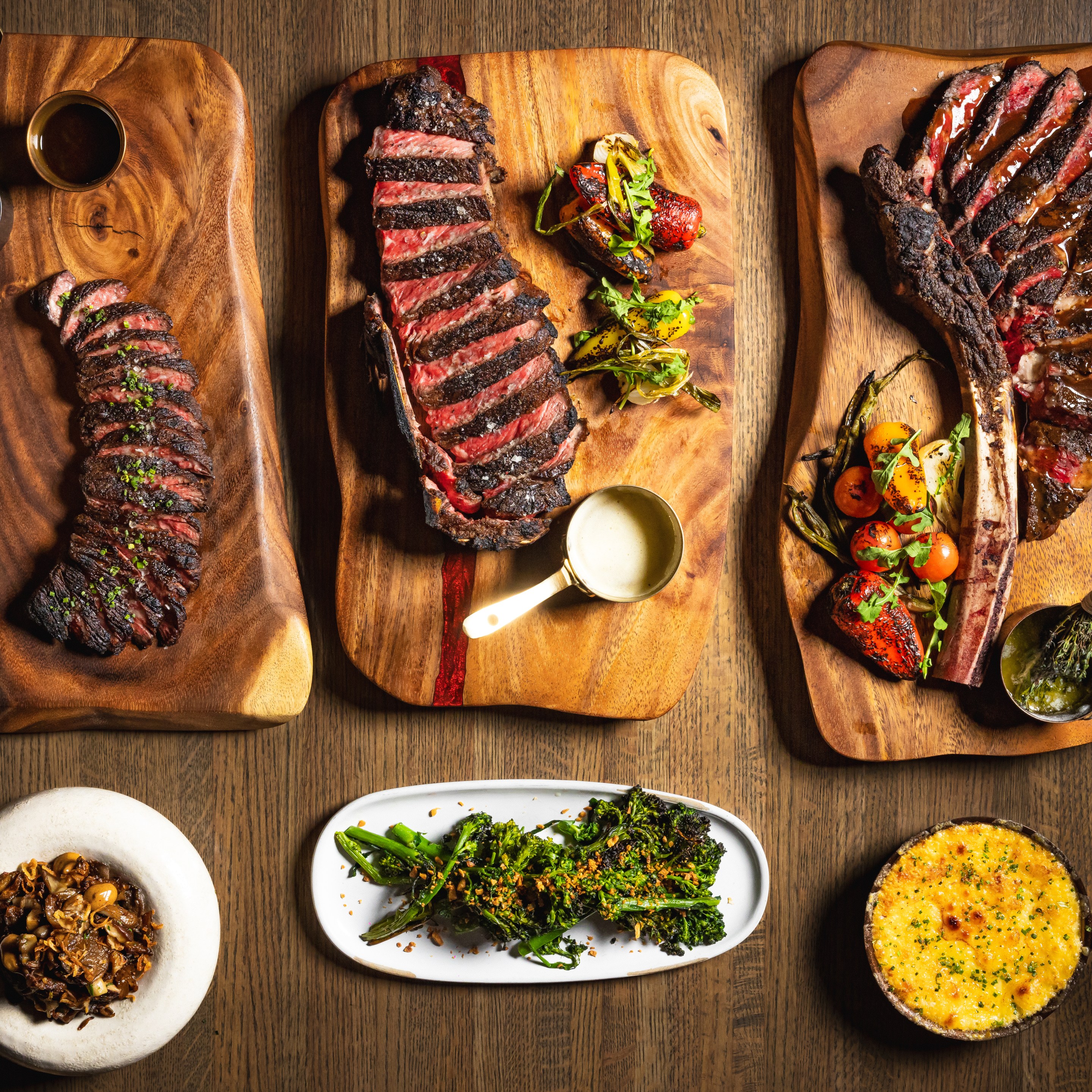 Wood fired steaks and side dishes served on wooden boards at Dēliz Italian steakhouse in Chicago.