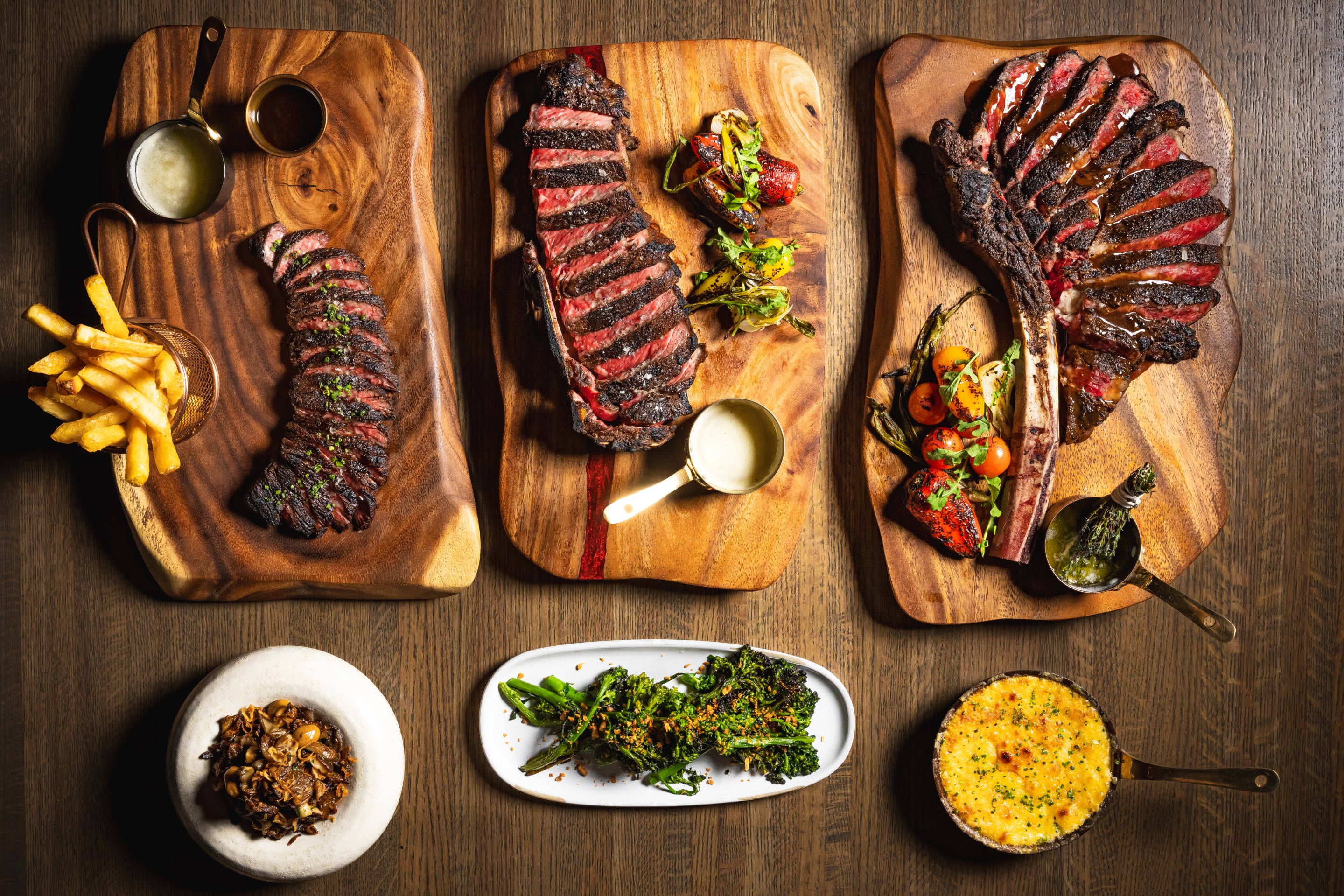 Wood fired steaks and side dishes served on wooden boards at Dēliz Italian steakhouse in Chicago.