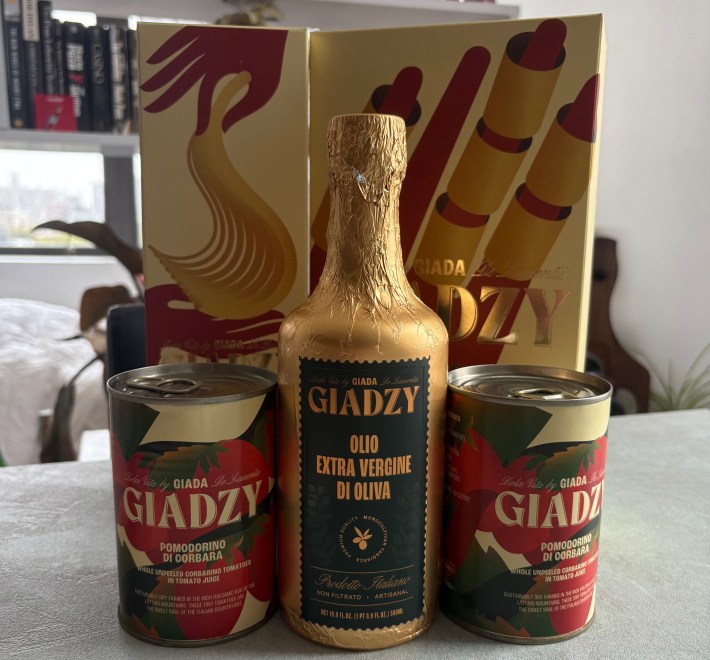 A gold Giadzy box with a bottle of olive oil and two cans of Corbarì tomatoes arranged in front.