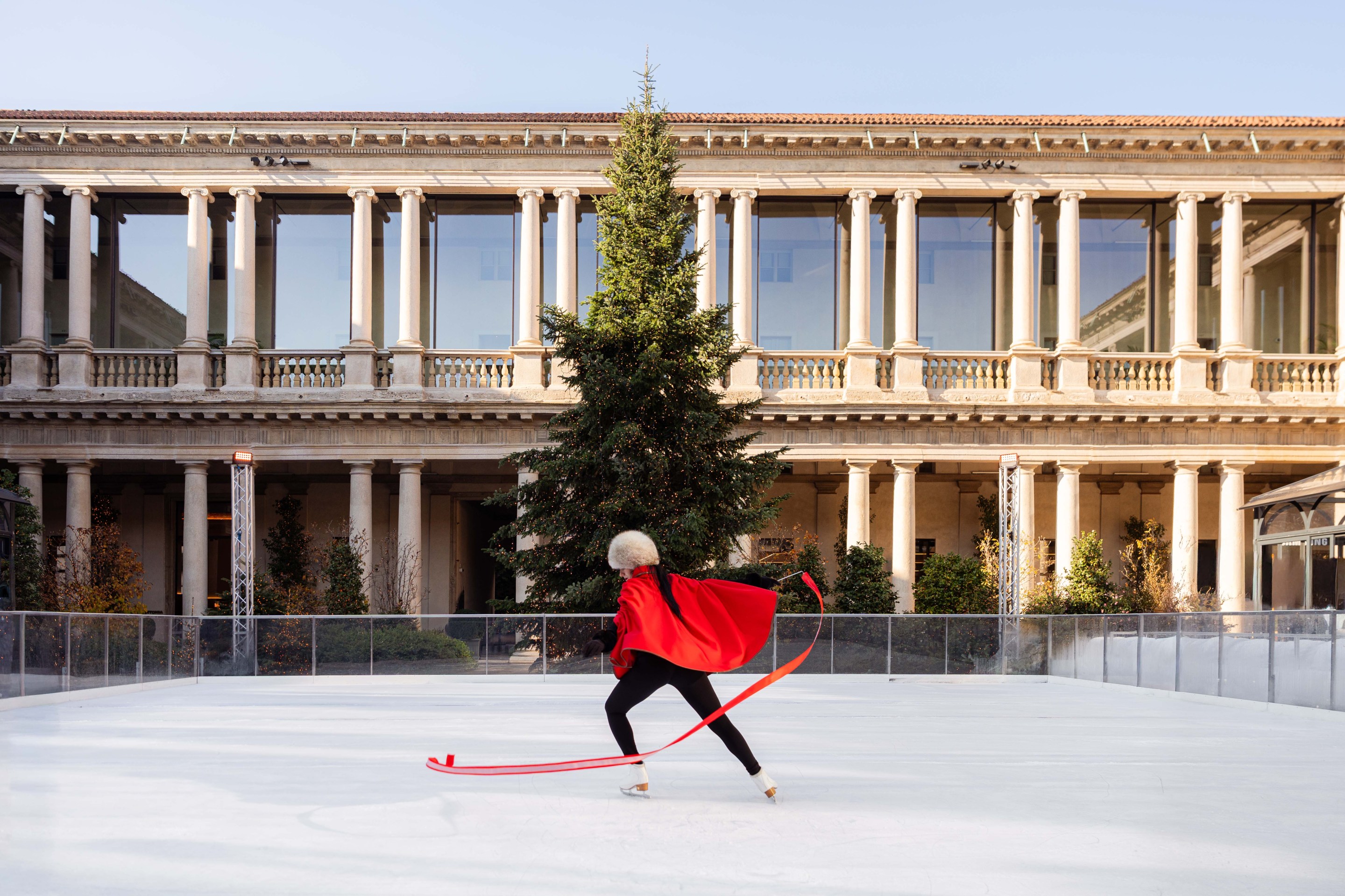 Ice skater performing in Portrait Milano courtyard with Christmas tree and hotel in background.