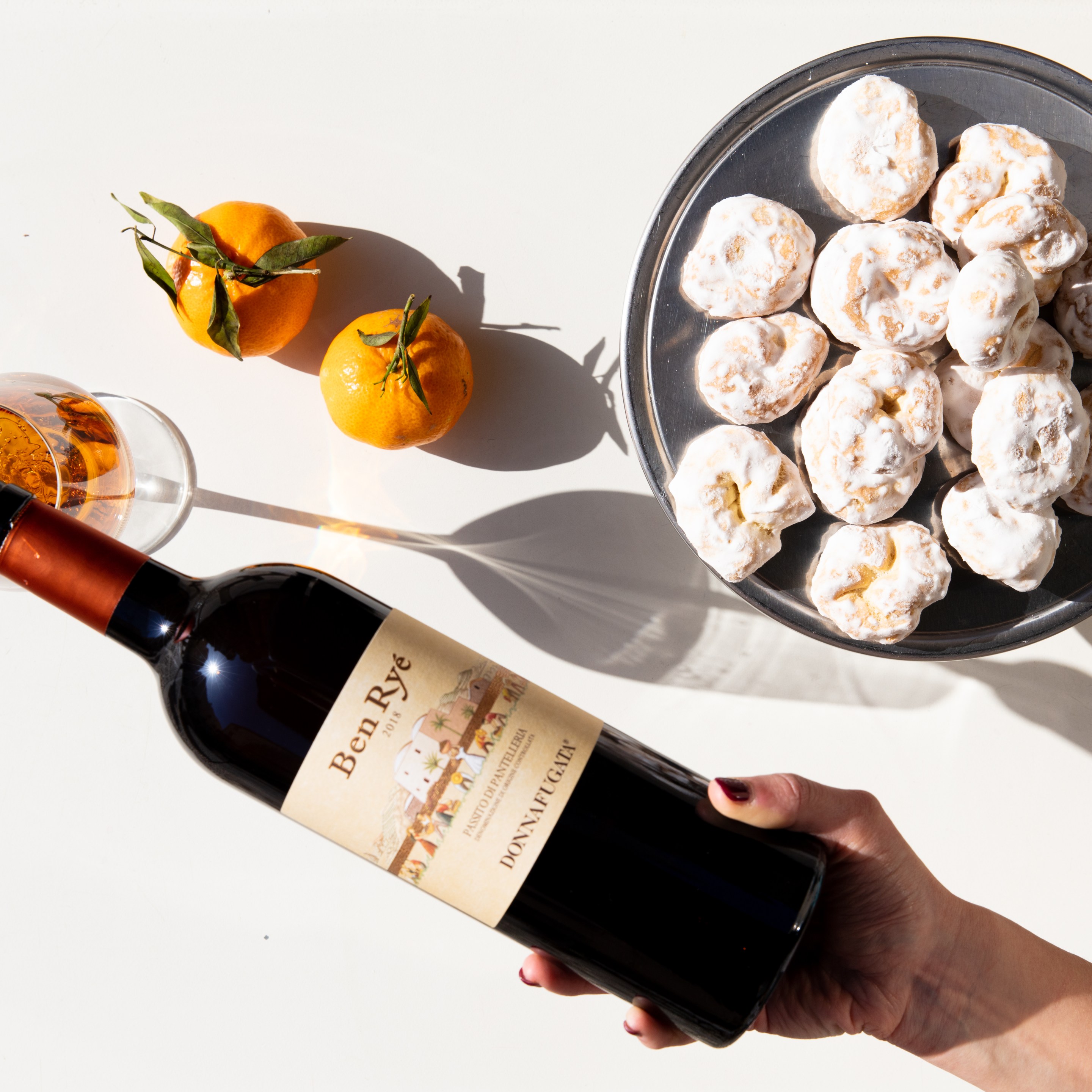 Bottle of Ben Ryé Passito di Pantelleria with citrus fruits, pastries, and a glass of dessert wine.