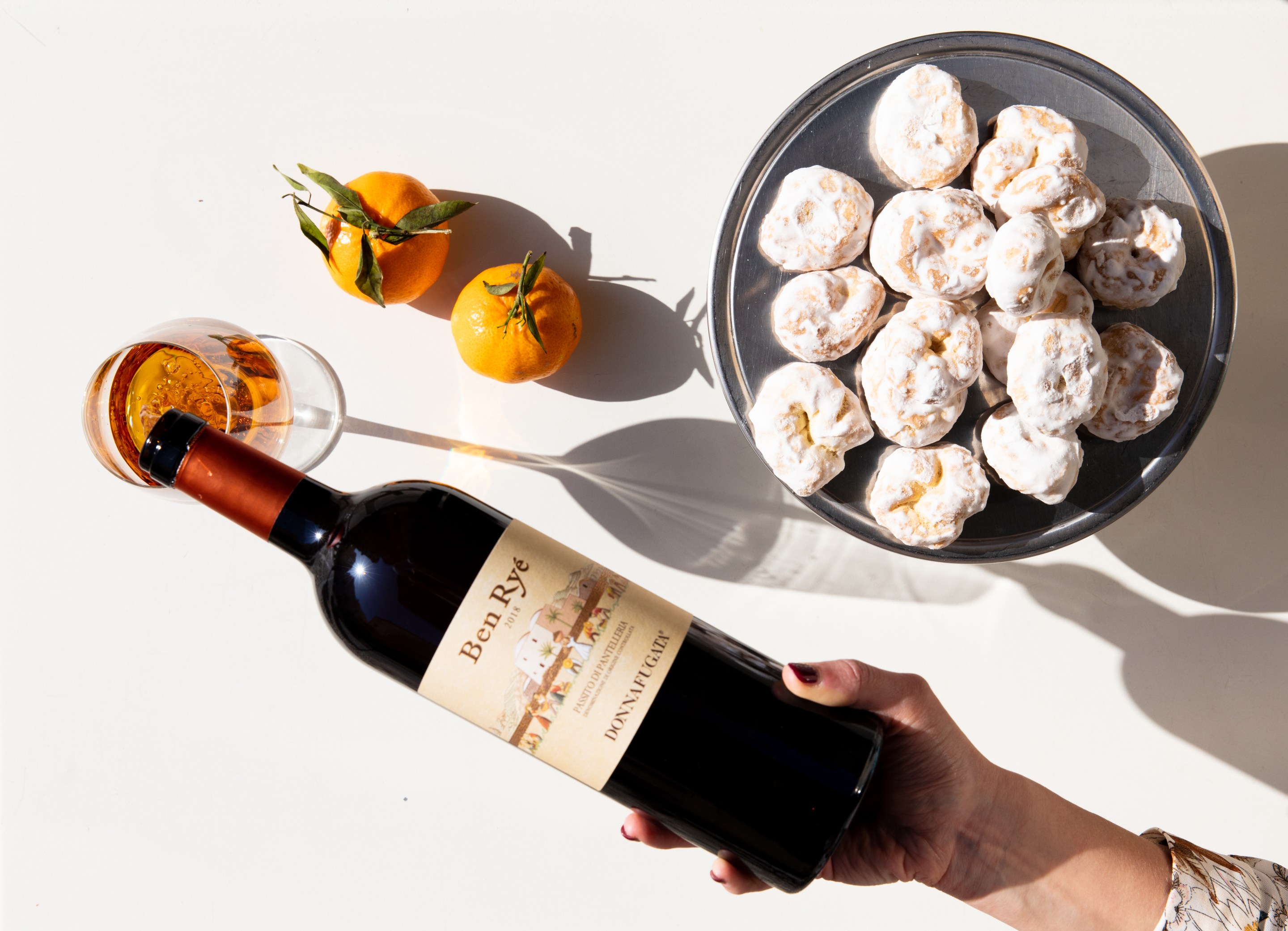 Bottle of Ben Ryé Passito di Pantelleria with citrus fruits, pastries, and a glass of dessert wine.