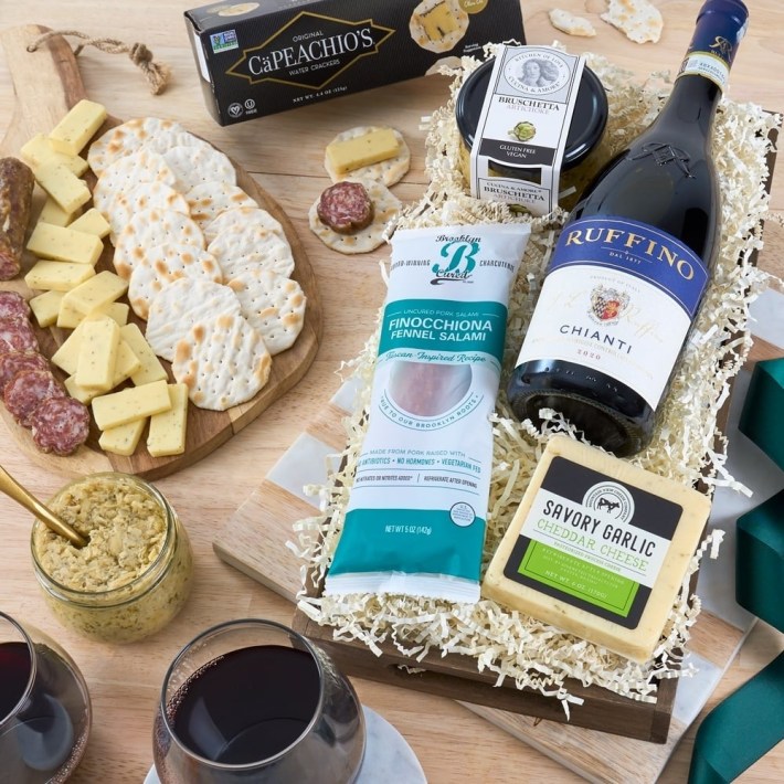 A wooden platter with salami, garlic cheddar, crackers, bruschetta spread, and a bottle of Ruffino Chianti.