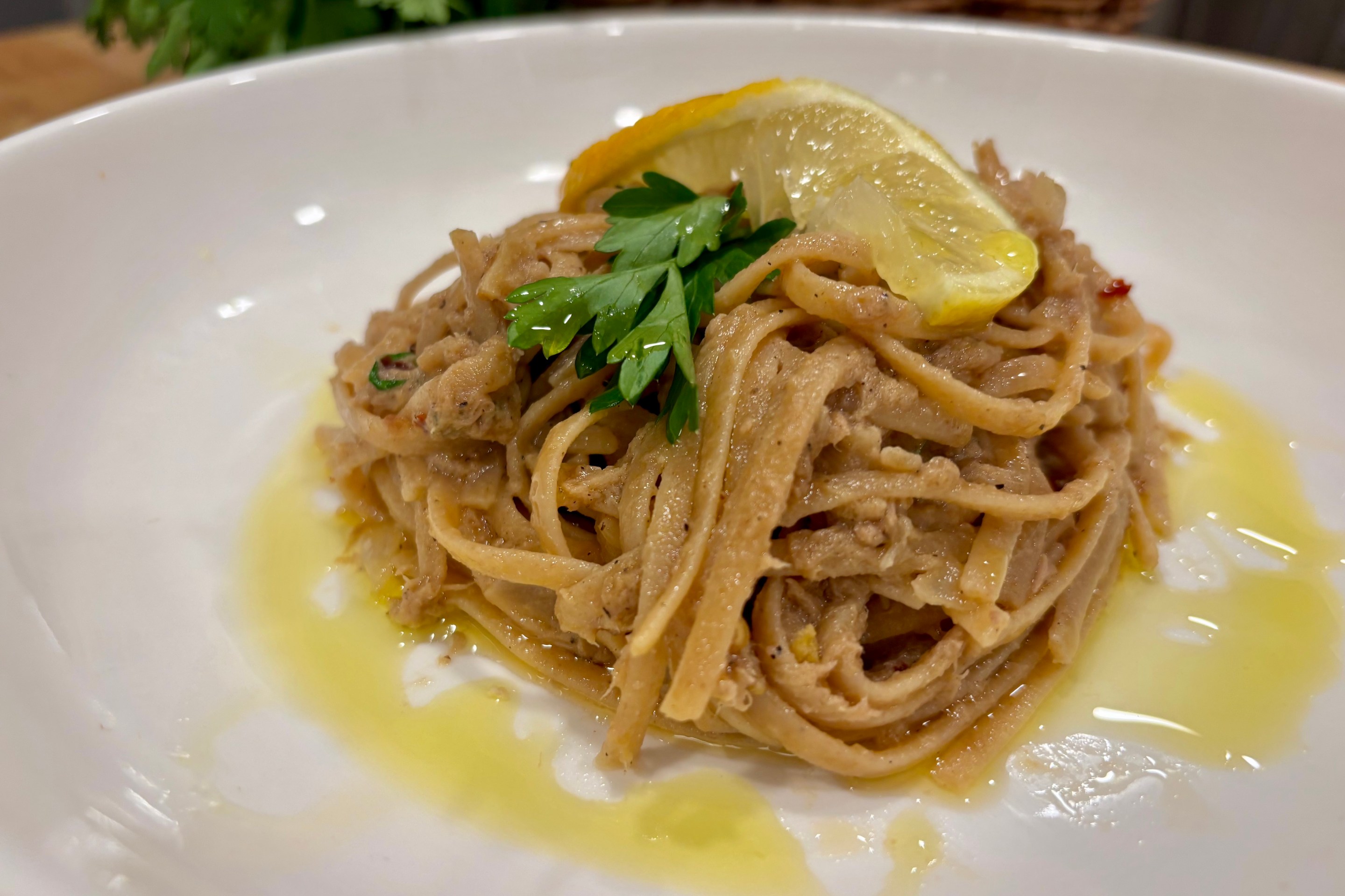 Blue-Zone Lemon Tuna Pasta with Garlic, Anchovy, and Parsley, topped with lemon and parsley in a white bowl.