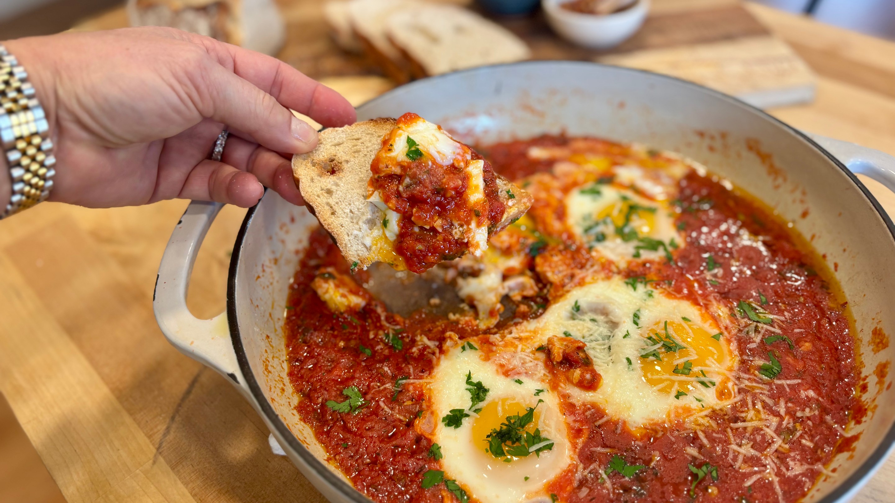 Eggs baked in a rich tomato sauce with pecorino and herbs in a white skillet, served with sliced crusty bread.