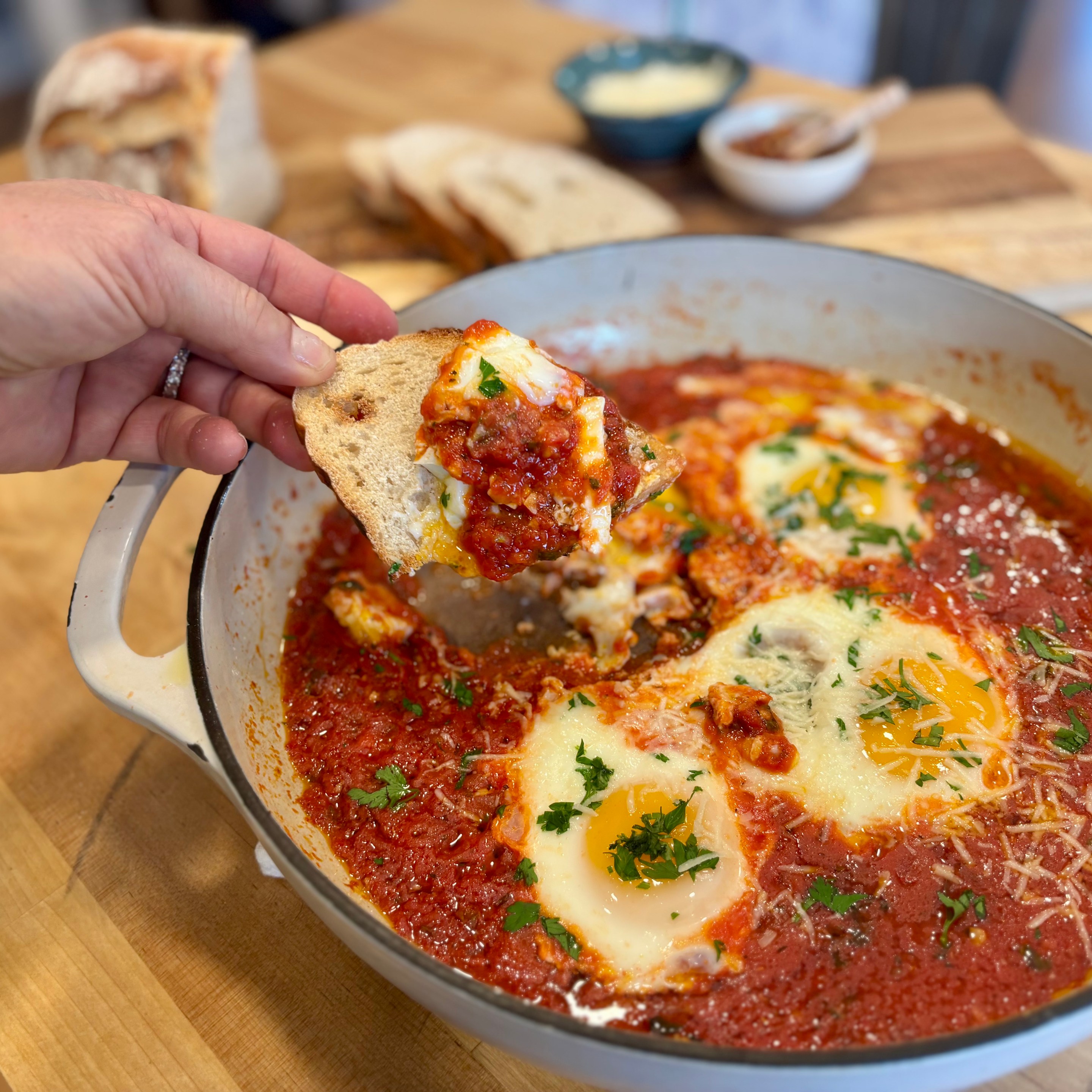 Eggs baked in a rich tomato sauce with pecorino and herbs in a white skillet, served with sliced crusty bread.