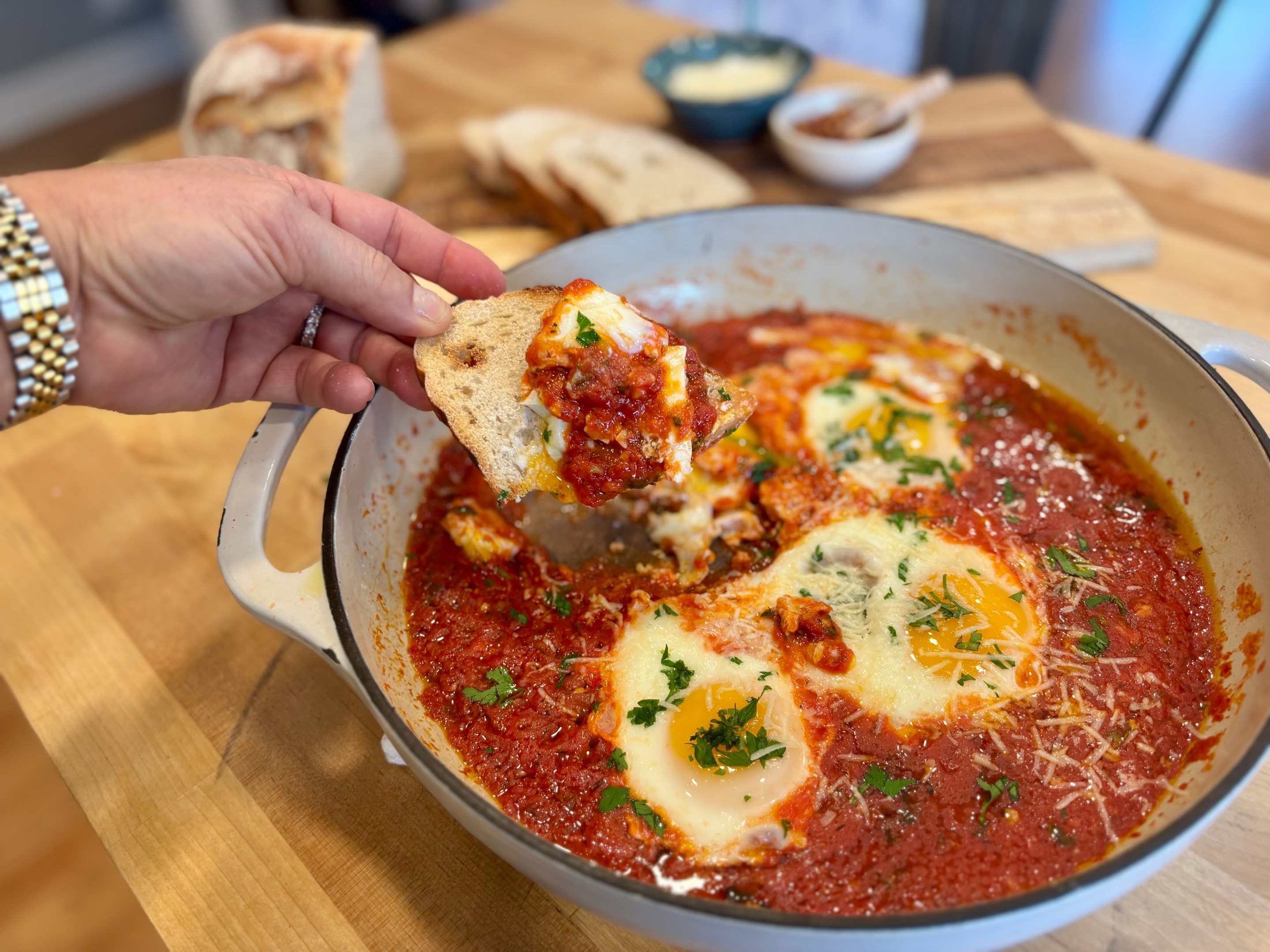 Eggs baked in a rich tomato sauce with pecorino and herbs in a white skillet, served with sliced crusty bread.