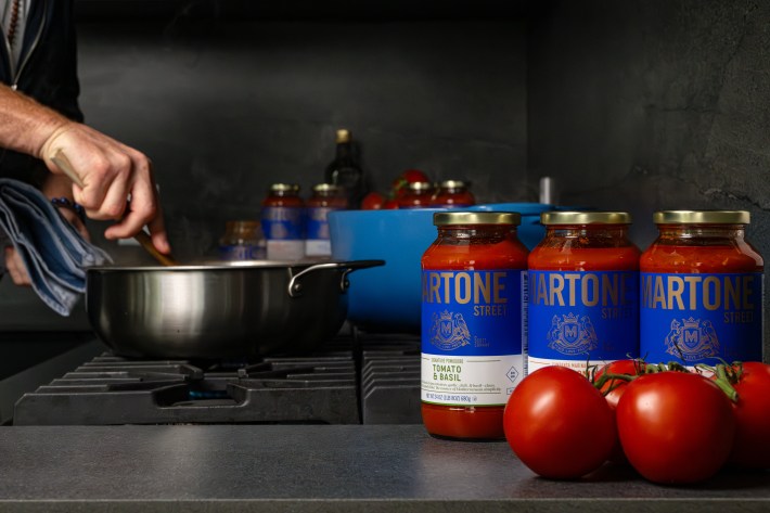 Martone Street tomato sauce jars next to a stovetop with fresh tomatoes