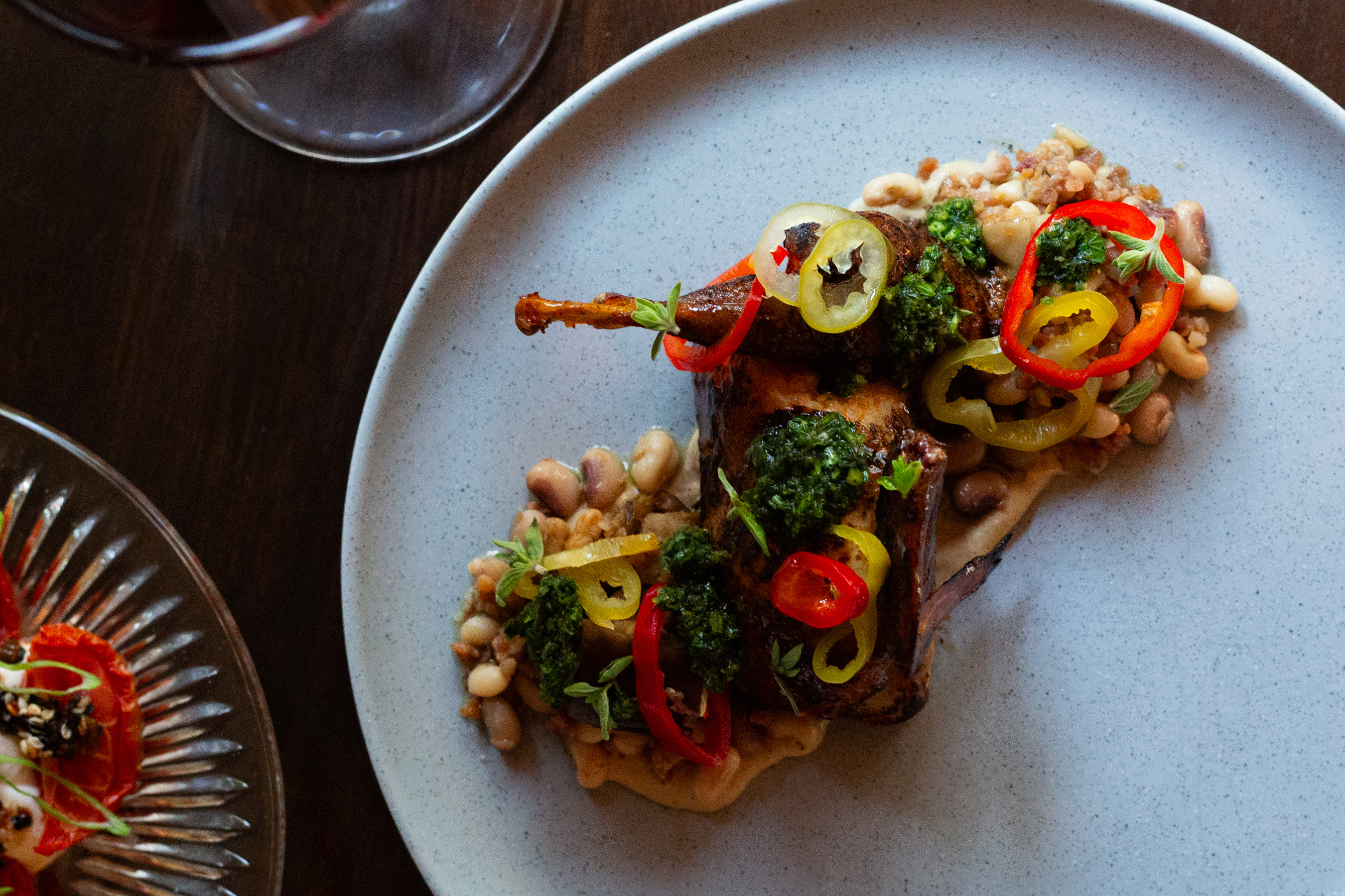 Roasted quail plated with beans, peppers, and herbs in a white dish. Courtesy of Poeta
